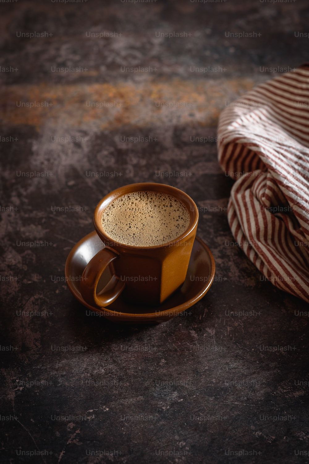 A cup of coffee on a table with a striped napkin. - Light brown