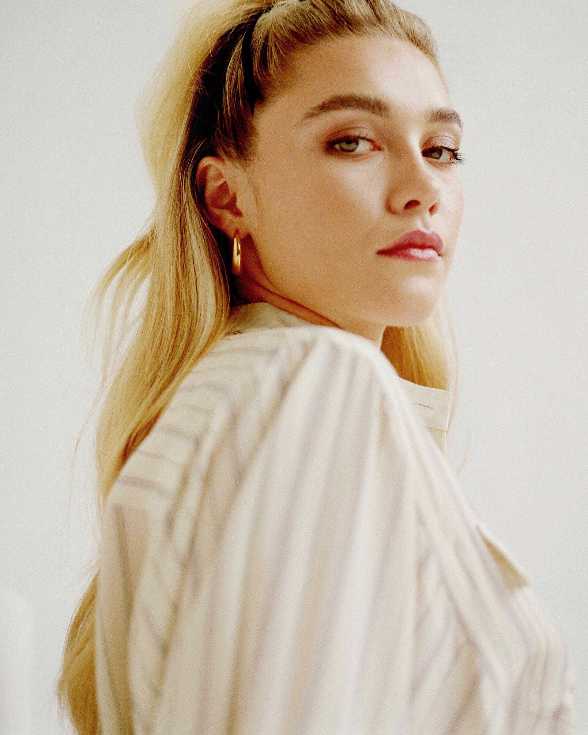 A woman with blonde hair in a ponytail wearing a white shirt. - Florence Pugh