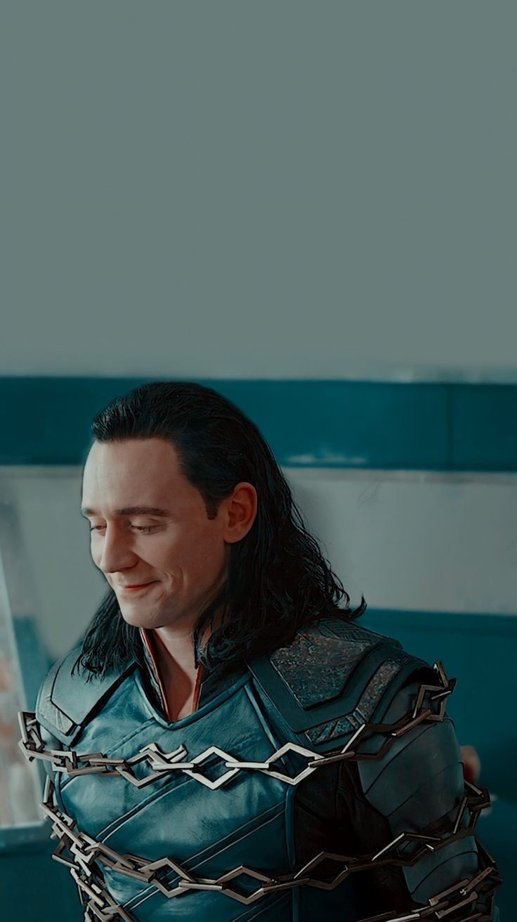 Tom Hiddleston as Loki in a scene from the TV series 'Loki', wearing a blue suit and looking down with a smile - Loki