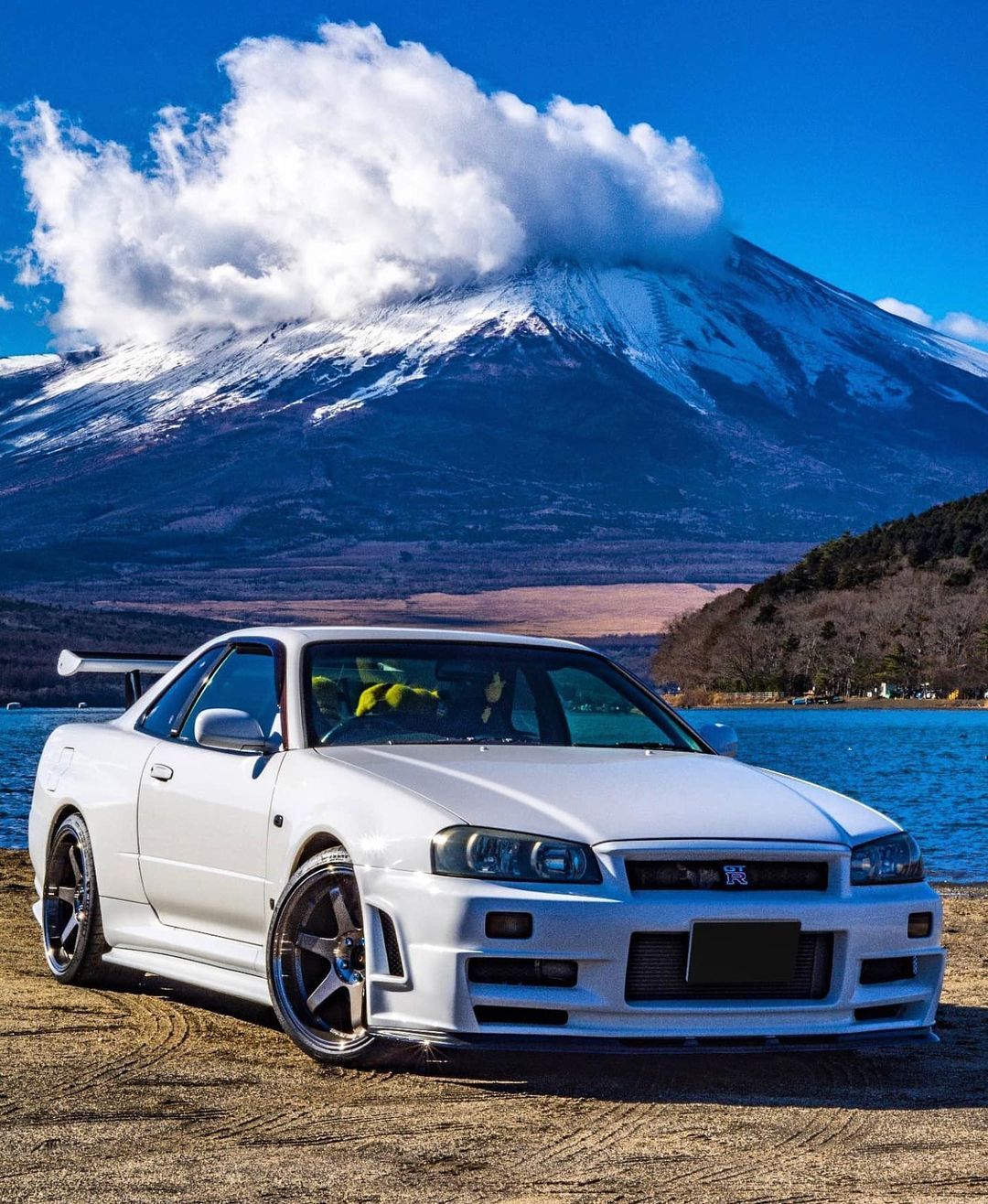 A white R34 skyline in front of a mountain - Nissan Skyline