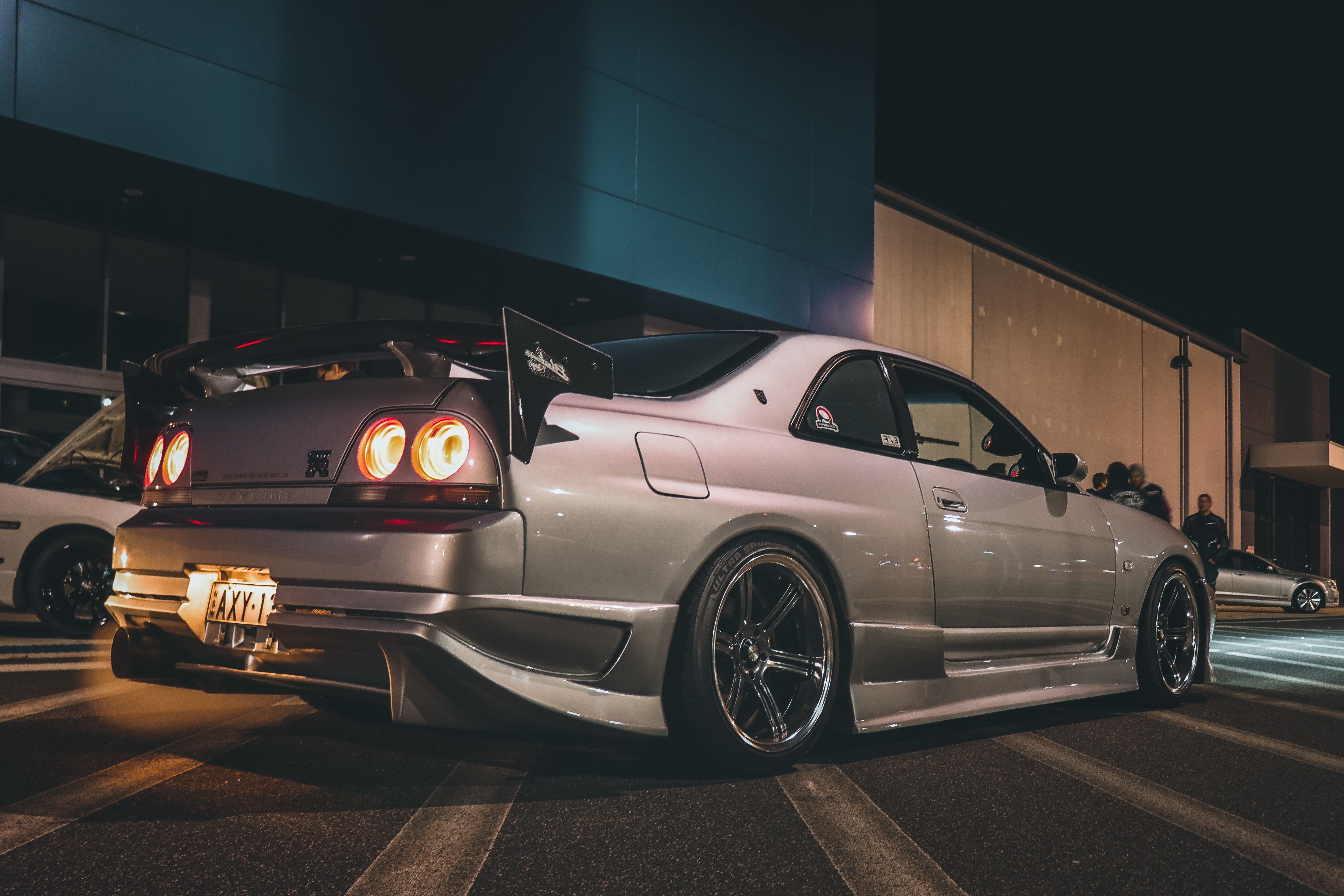 A silver R34 GTR with a massive wing and a plate that says 