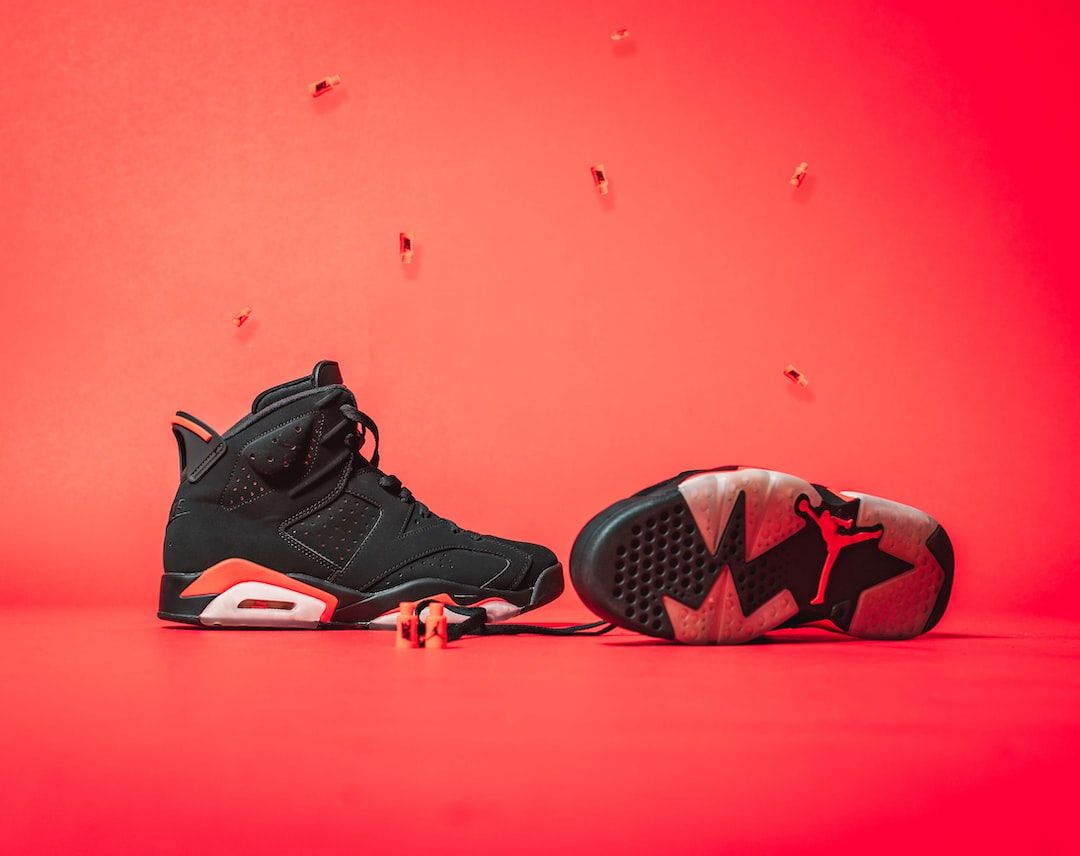 A pair of black and red Nike sneakers sit on a red background. - Air Jordan 6