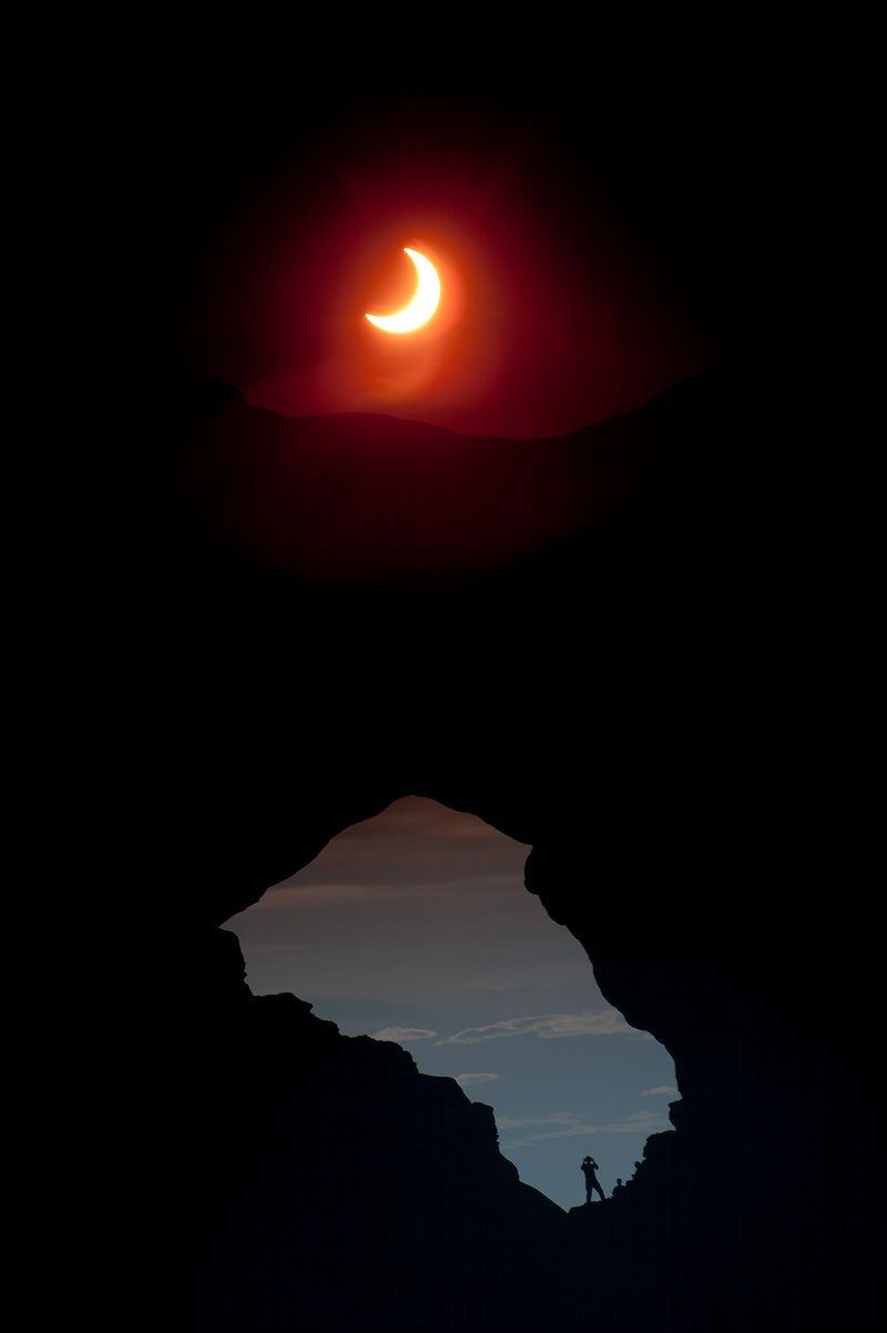 A man stands on a mountain peak as the moon partially covers the sun. - Eclipse