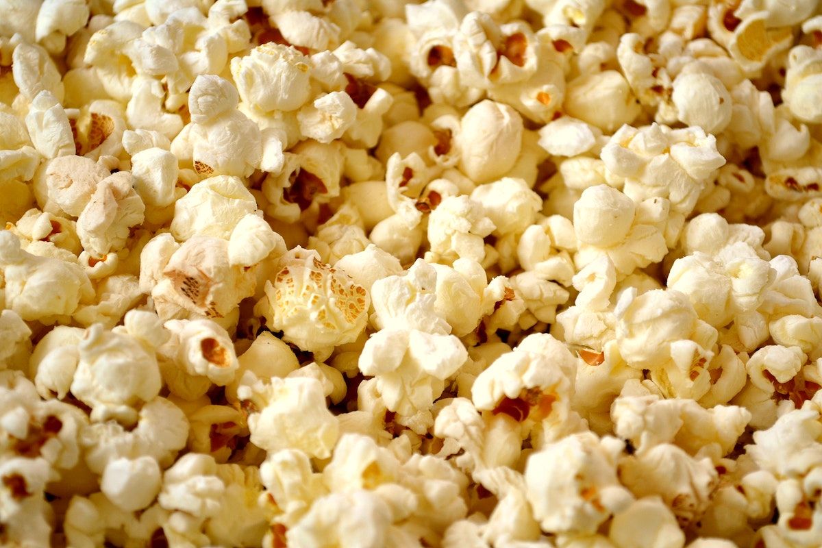 A close up of popcorn, with a pile of it in the foreground and a single kernel slightly out of place. - Popcorn