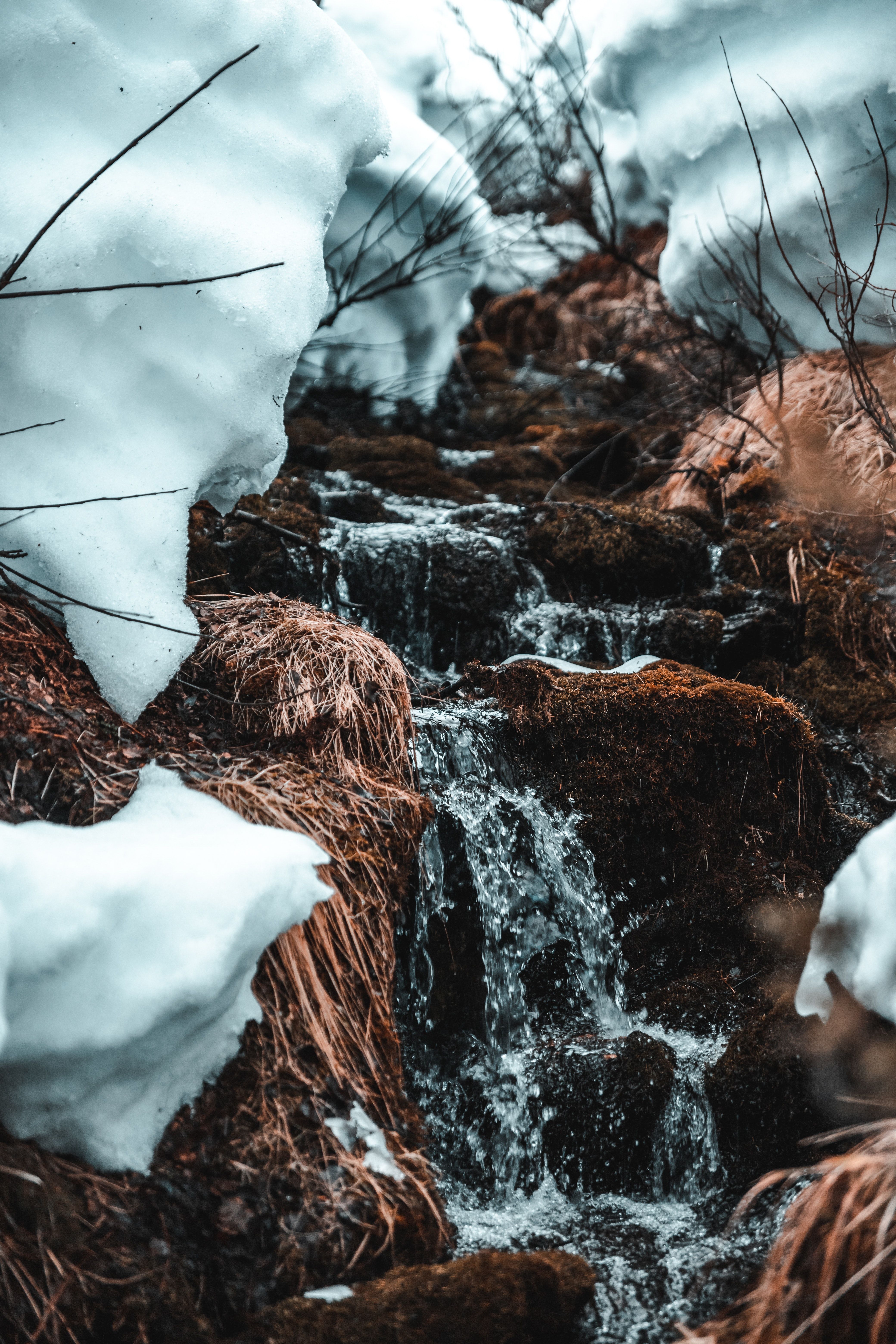 A stream of water flows through the snow covered rocks. - Waterfall