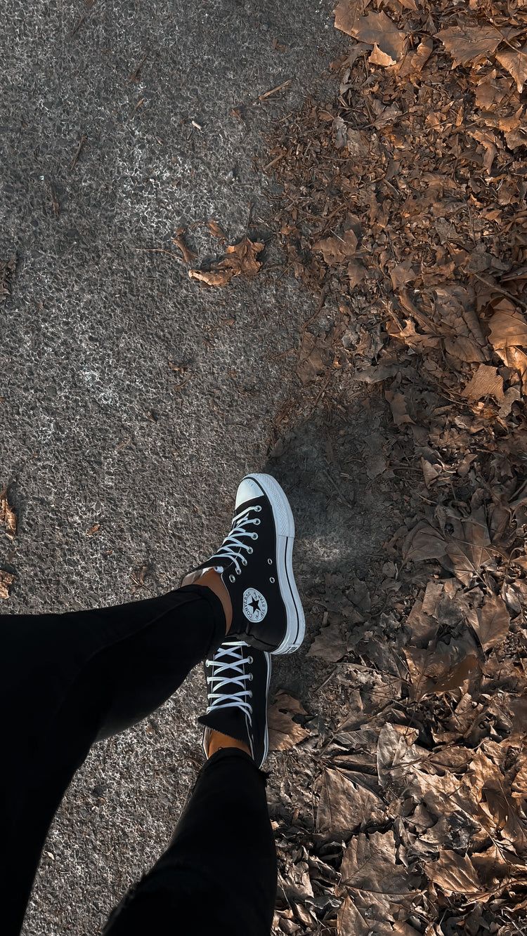 A person wearing black jeans and black and white converse sneakers. - Converse