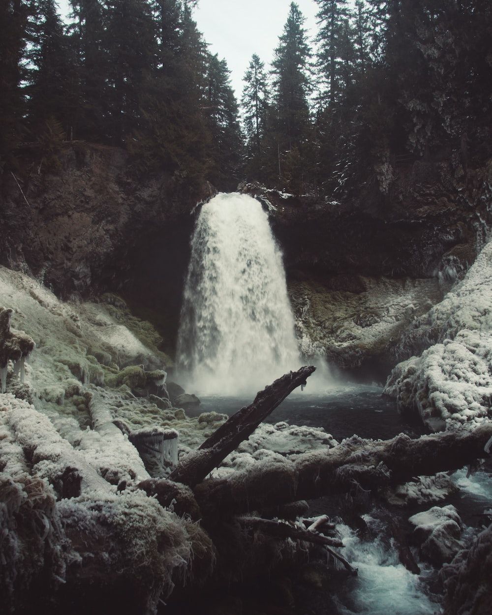 A waterfall with snow on the ground and trees in the background photo