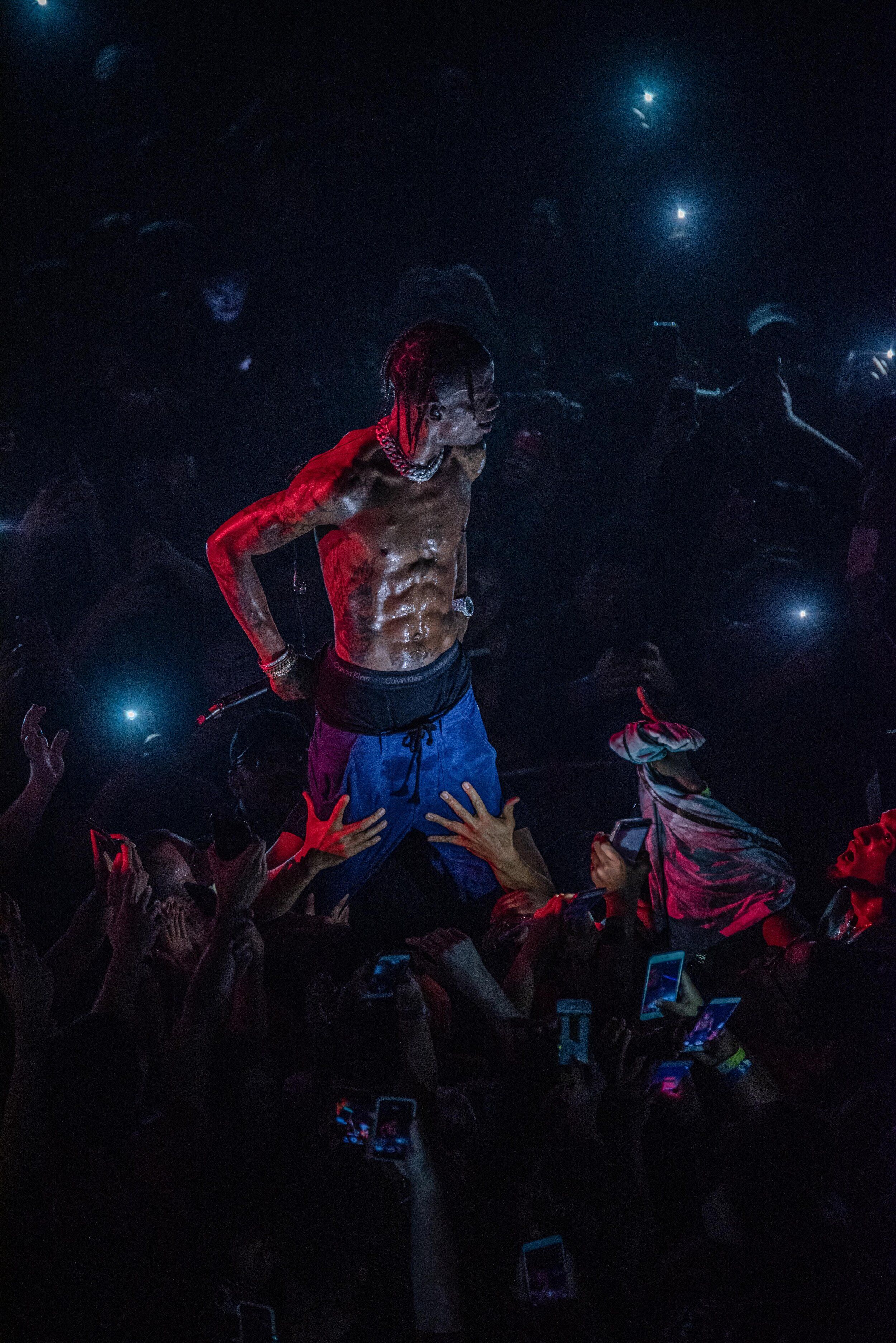 A shirtless man standing on top of a crowd of people in a dark room with his hands on his hips. - XXXTentacion