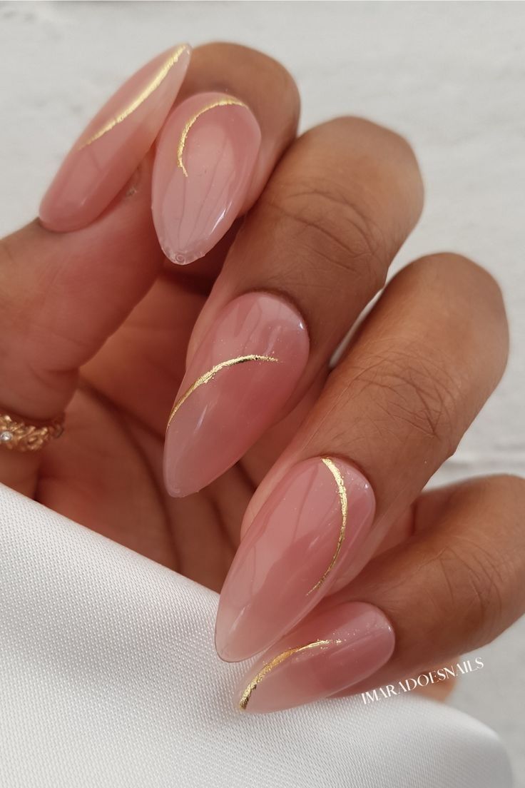 A woman's hand with long, stiletto nails painted in a light pink color and adorned with gold stripes. - Nails
