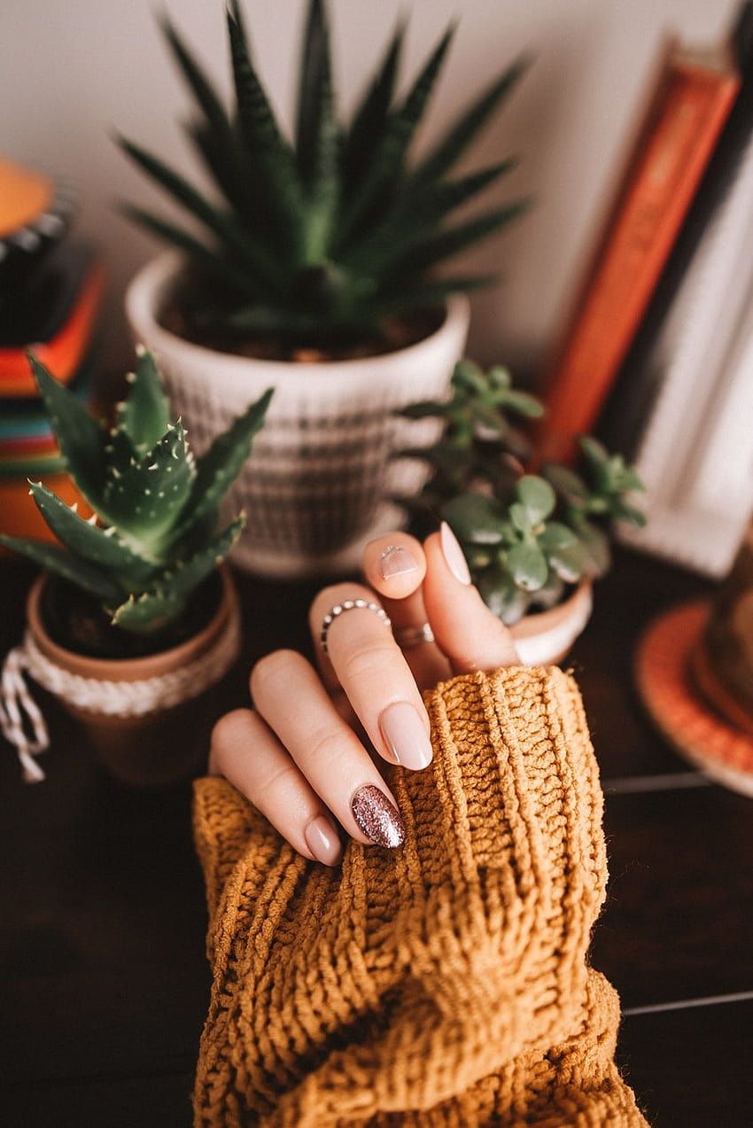 A woman's hand with a gold and pink manicure holding a gold sweater - Nails