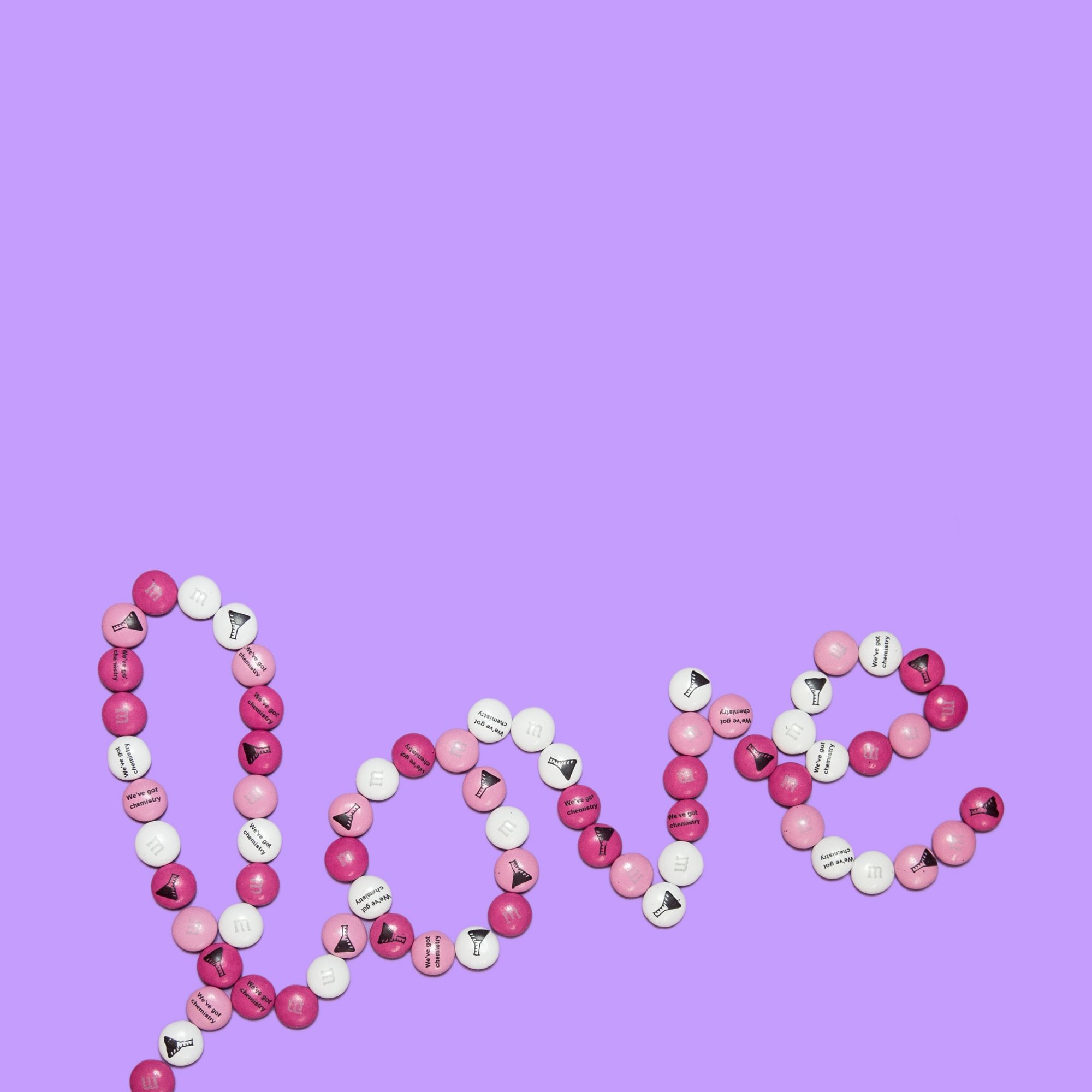 The word love spelled out with pink and white candy on a purple background - Chemistry