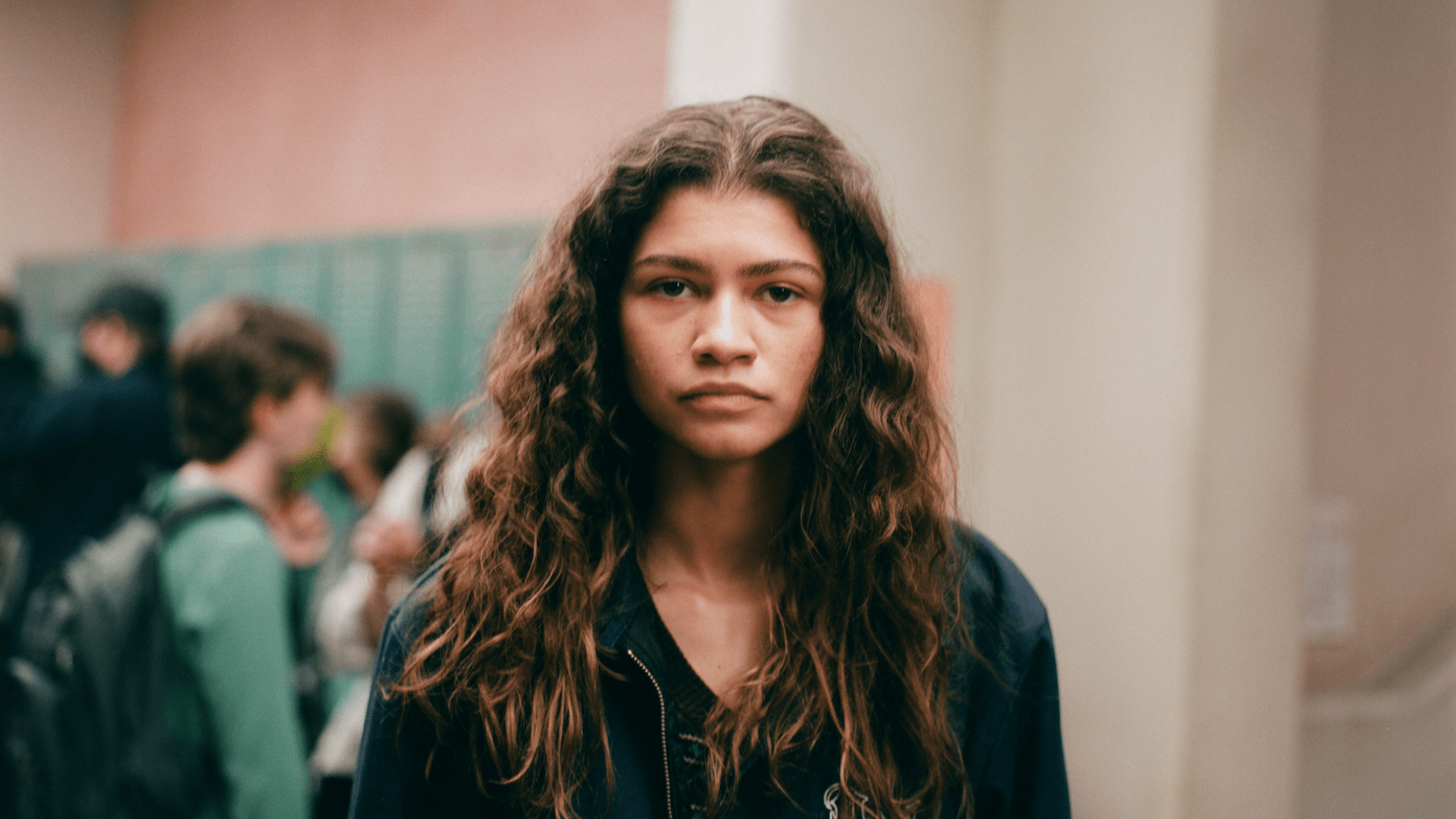 A girl with long curly brown hair looks directly at the camera. - Zendaya
