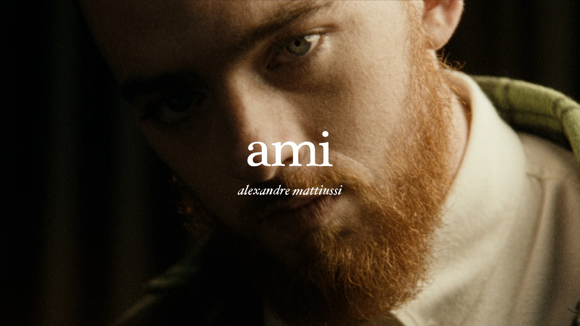 A man with a red beard looks into the camera. The word 