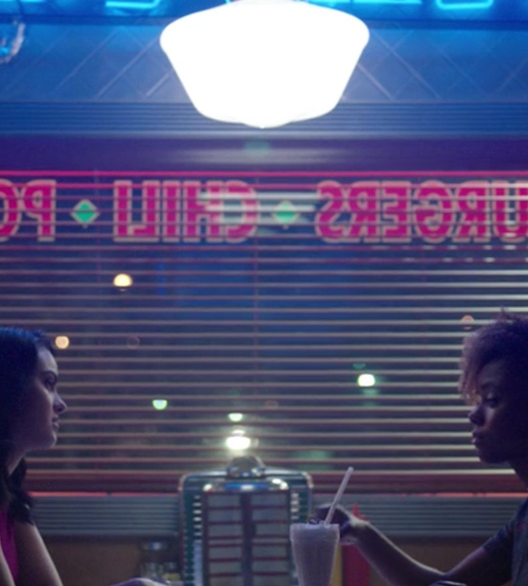 Two characters from Riverdale sit at a diner table under a neon sign - Riverdale