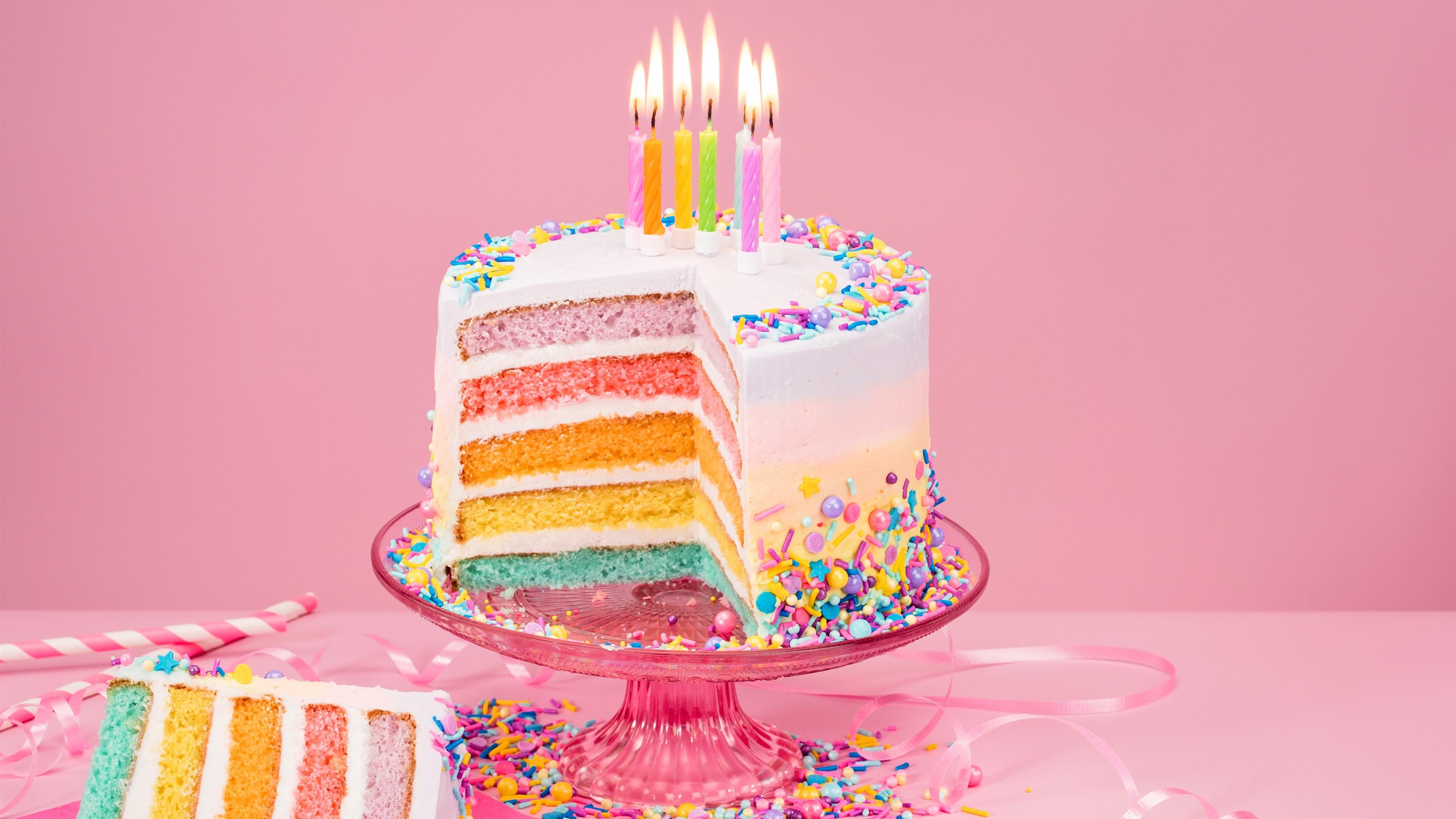 A slice of a six-layer rainbow cake with candles on a pink background - Cake