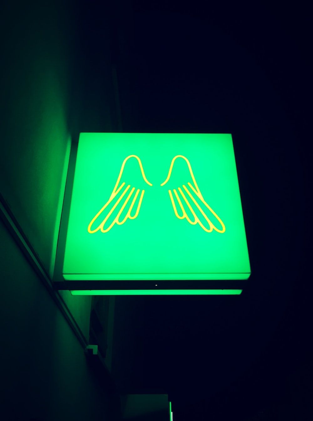 A green neon sign with a pair of wings. - Wings