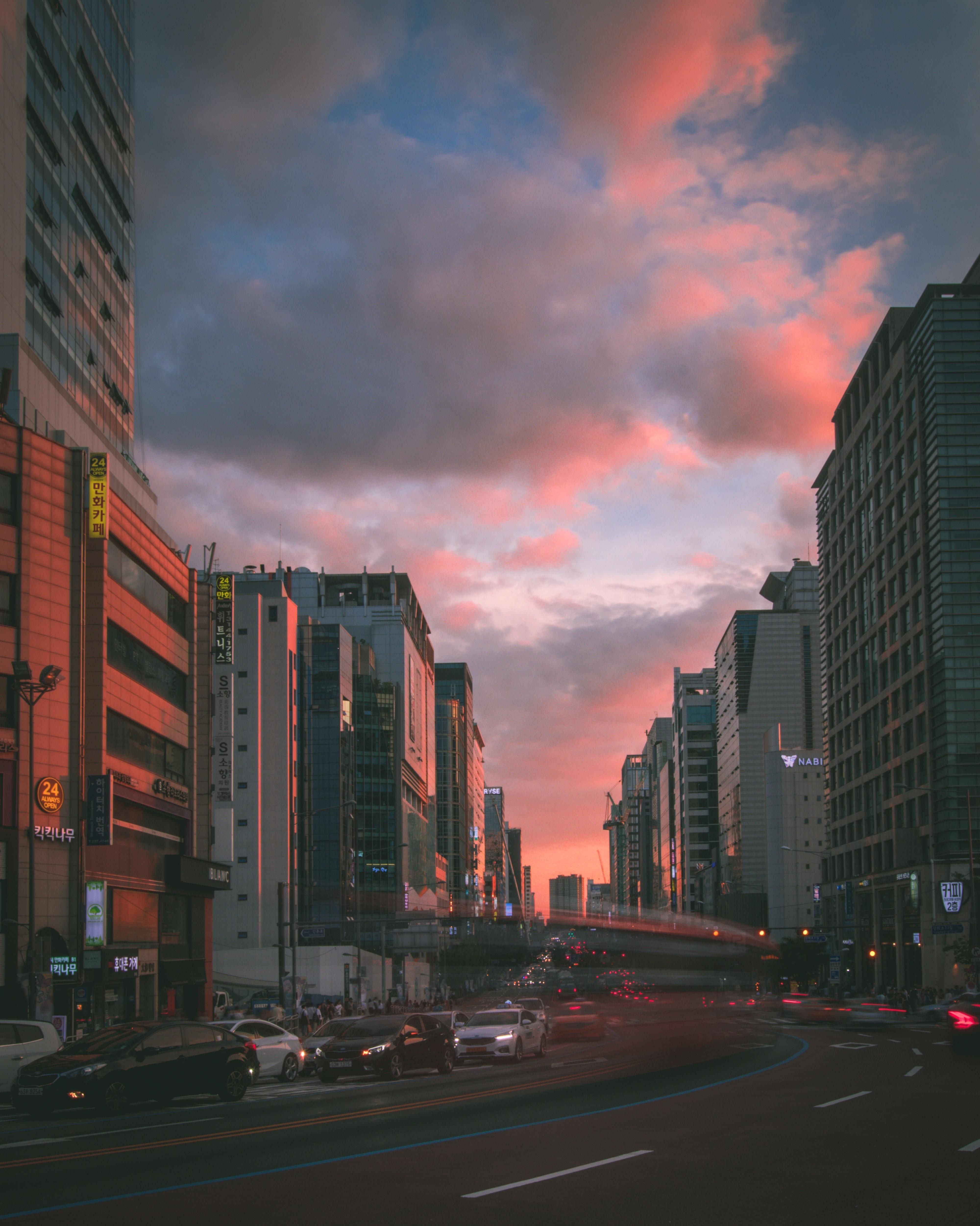 A city street with tall buildings and a pink sky. - Seoul