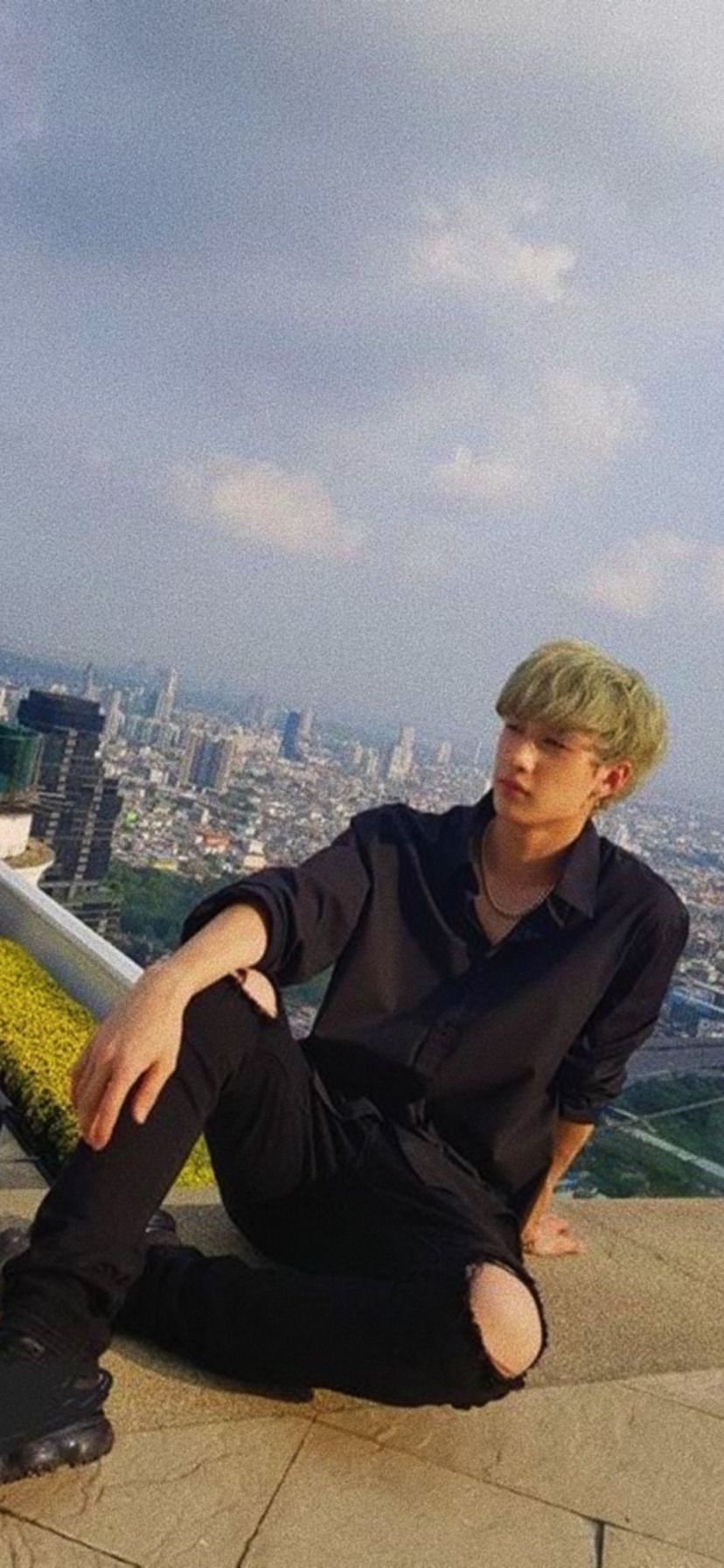 A person in black shirt sitting on the edge of building - Bang Chan