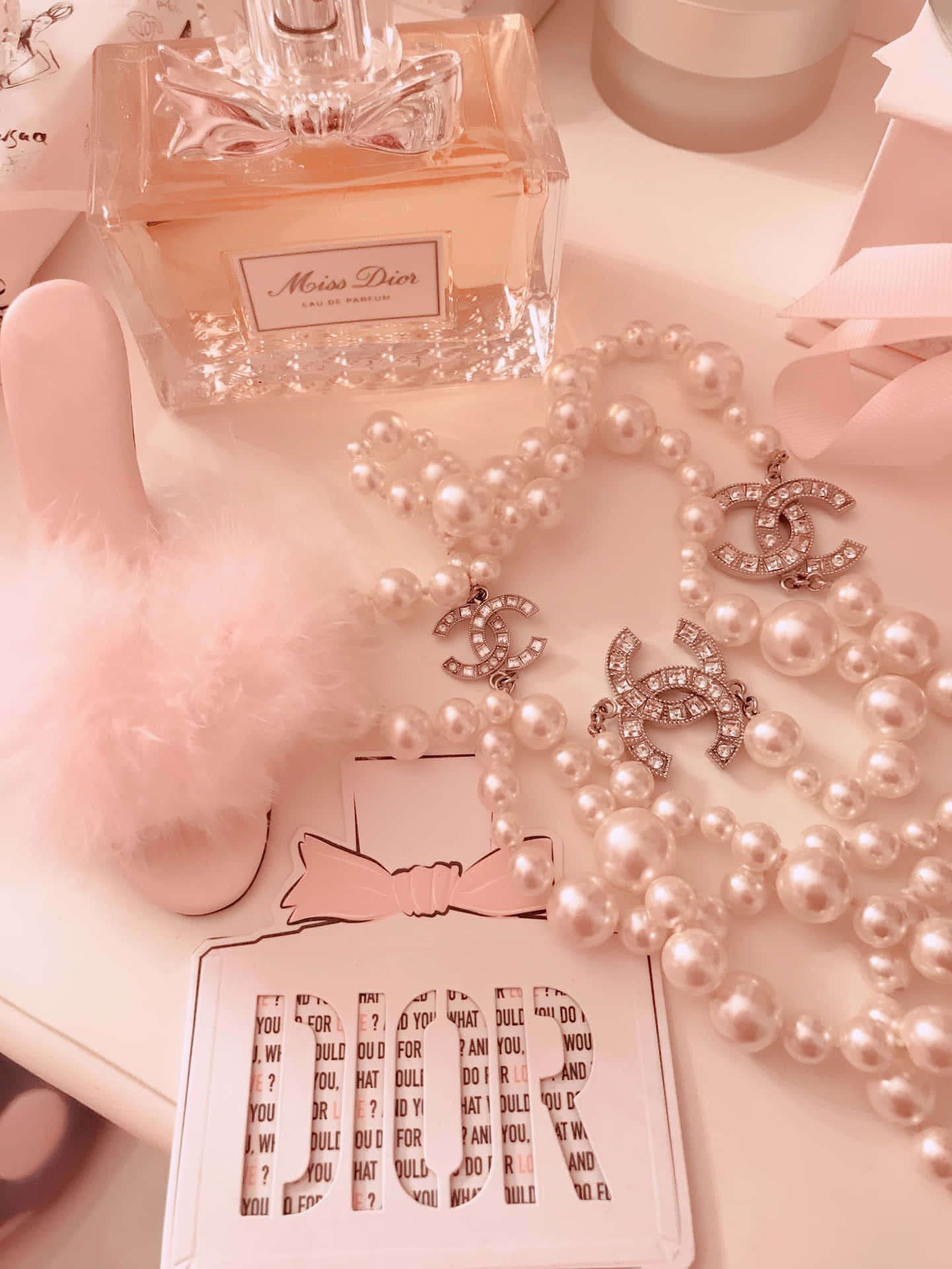 A flat lay of a white table with Miss Dior perfume, pearls, a white fluffy bunny and a white chanel brooch. - Bling, Dior, boujee