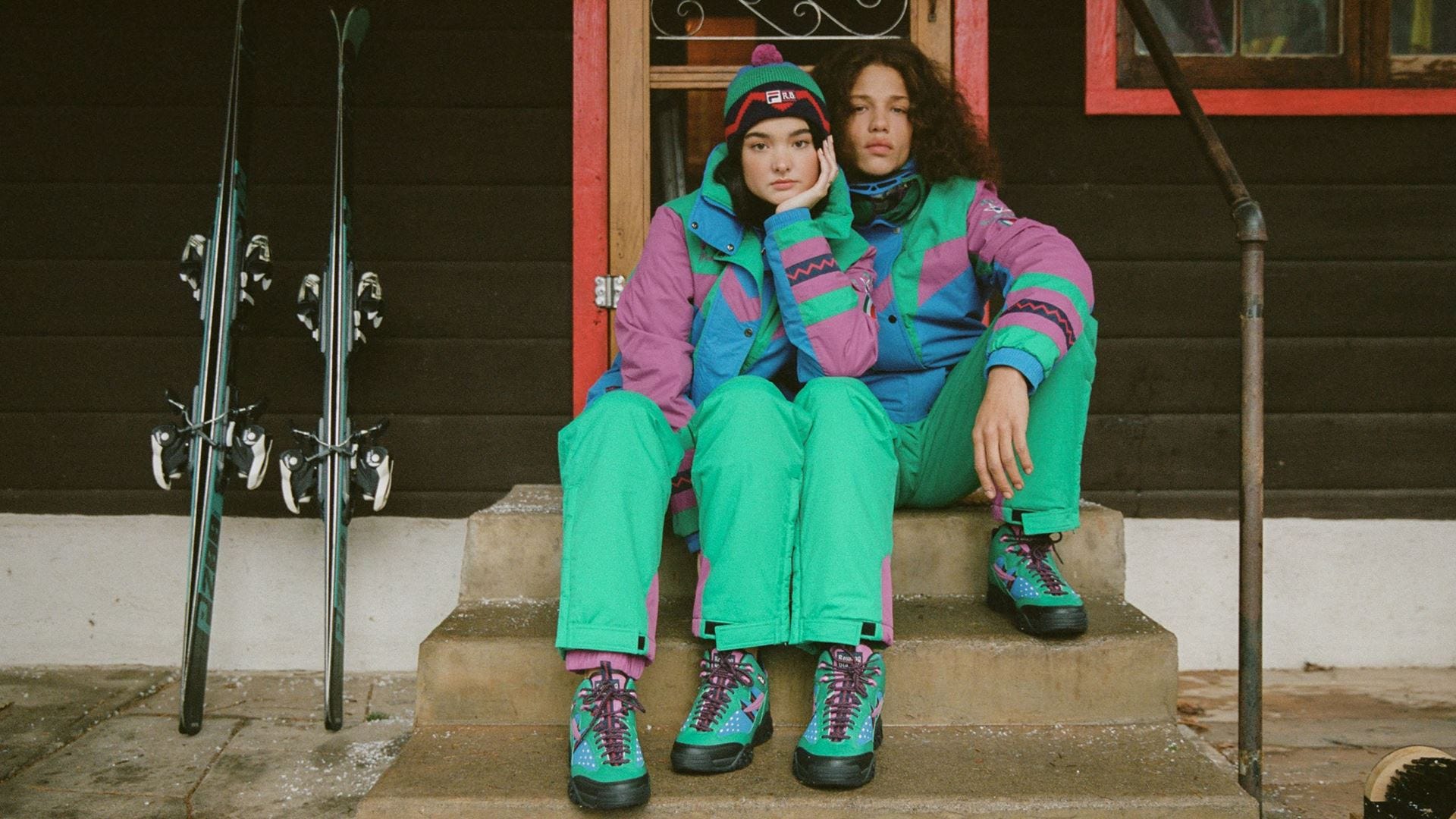 Two women sitting on the steps of a ski lodge wearing The North Face x Gucci ski jackets and boots - Gorpcore