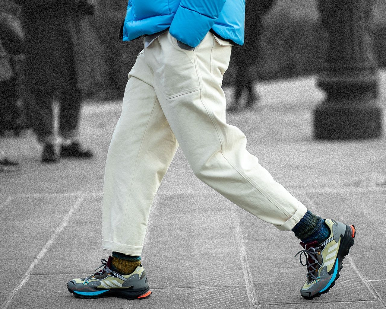A person wearing a blue jacket and white pants walking down a street. - Gorpcore