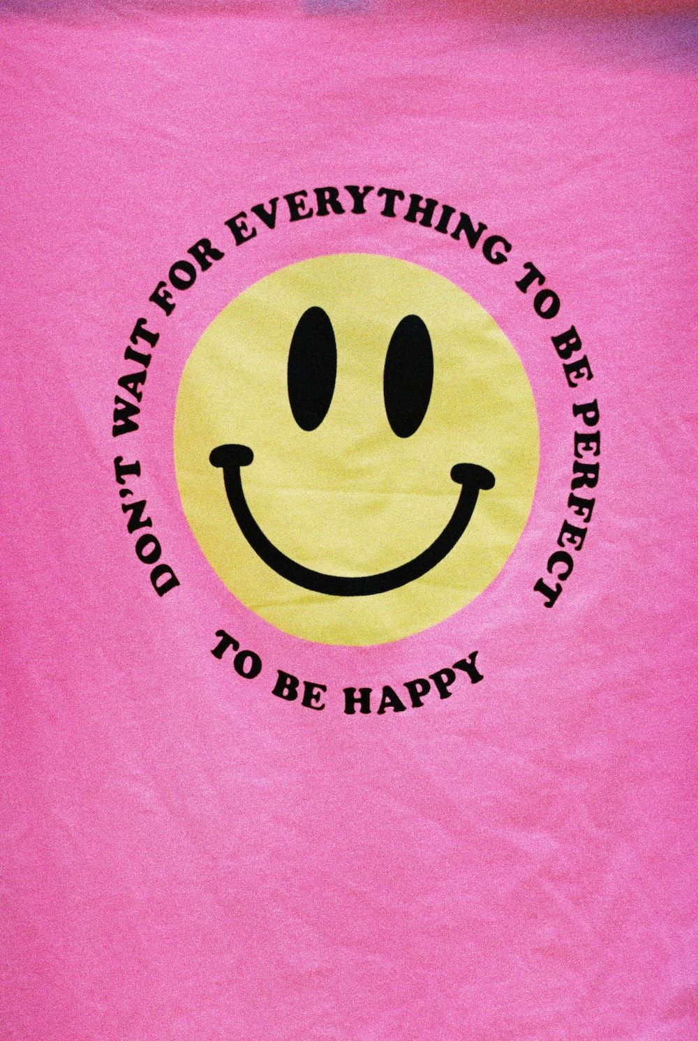 A pink t-shirt with a yellow smiley face on it. - Smiley