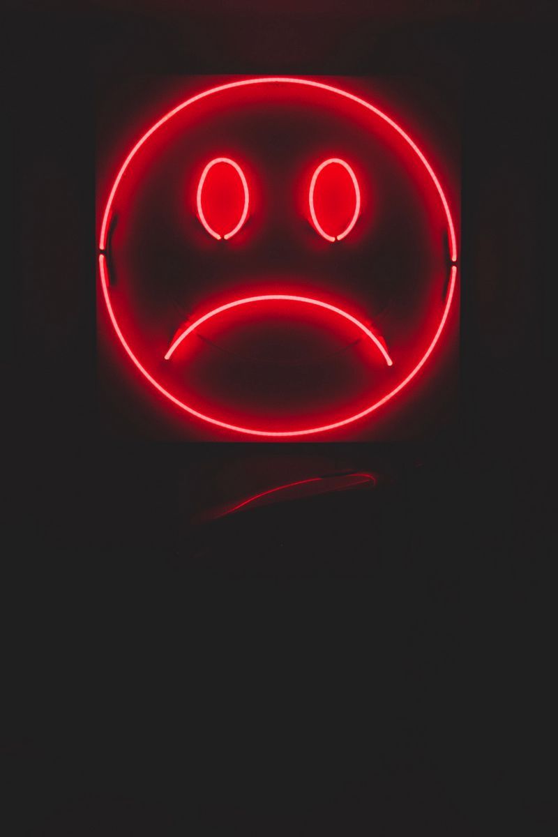 A red neon sign of a sad face. - Neon red