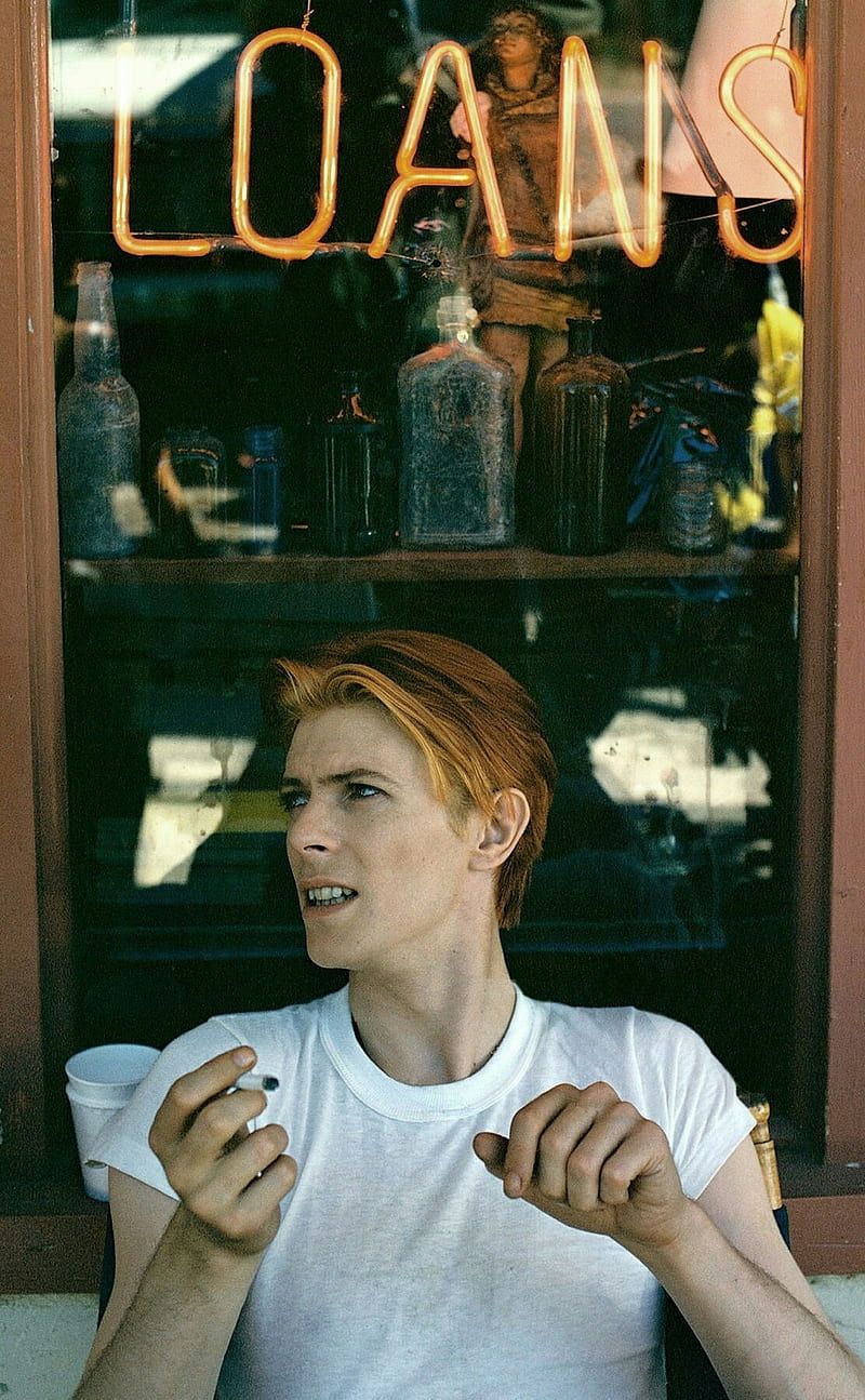 David Bowie with red hair sitting in front of a window - David Bowie