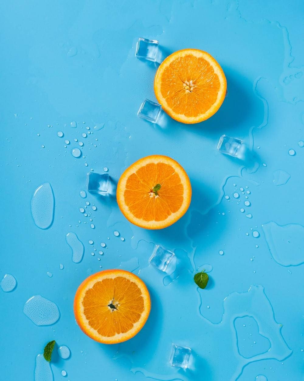 Sliced oranges on a blue background with ice cubes - Pastel orange