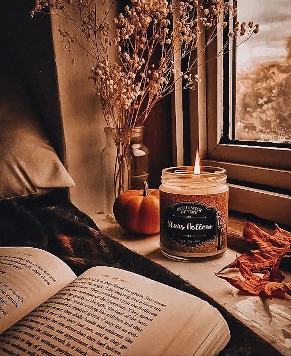 A book, a candle, a pumpkin, and some flowers sit on a windowsill. - Vintage fall