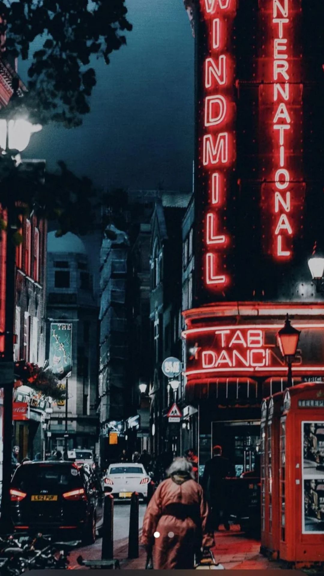 A couple walking down the street at night in front of a red neon sign. - IPhone red