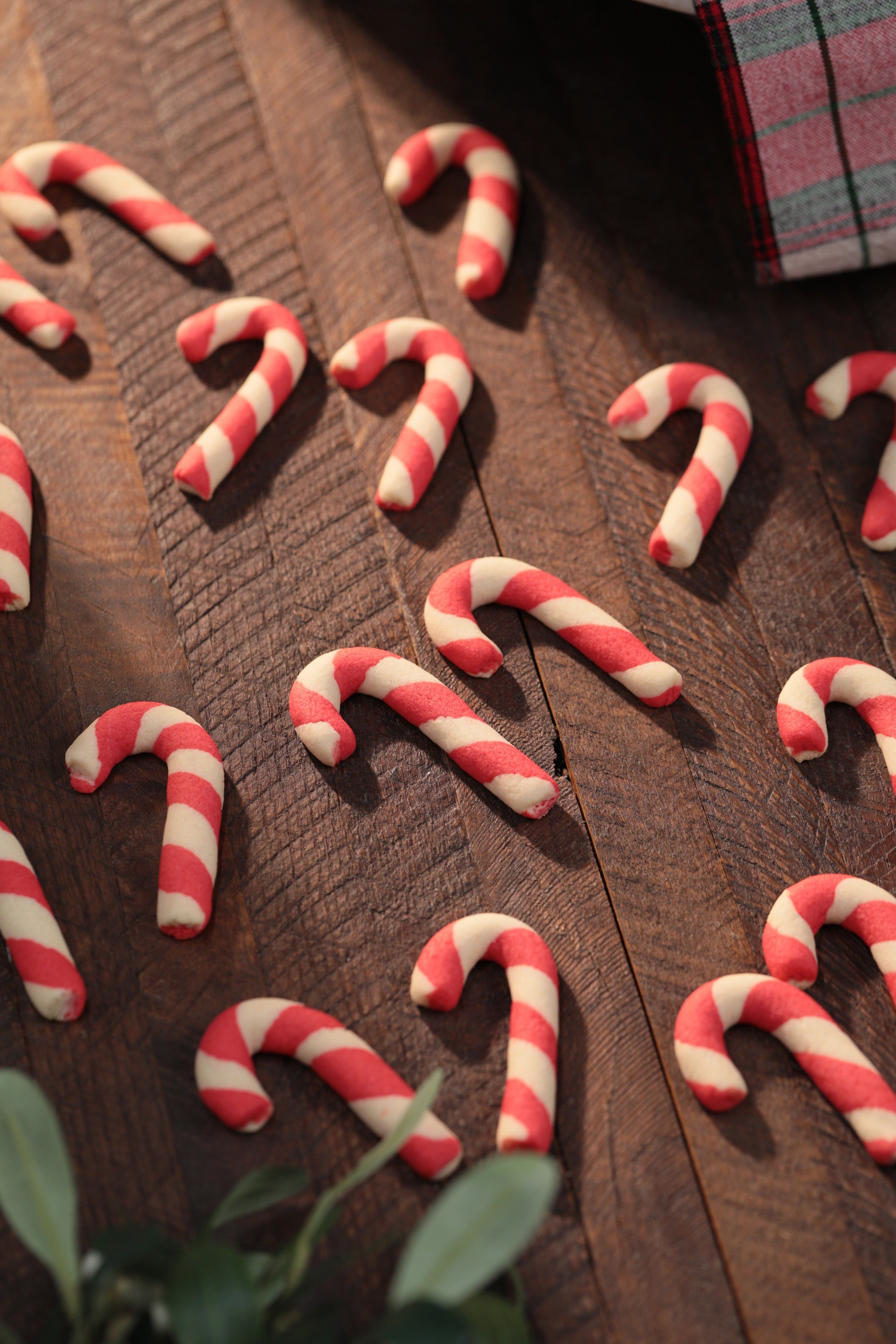 A rustic wooden table with a diagonal arrangement of red and white striped candy canes. - Candy cane