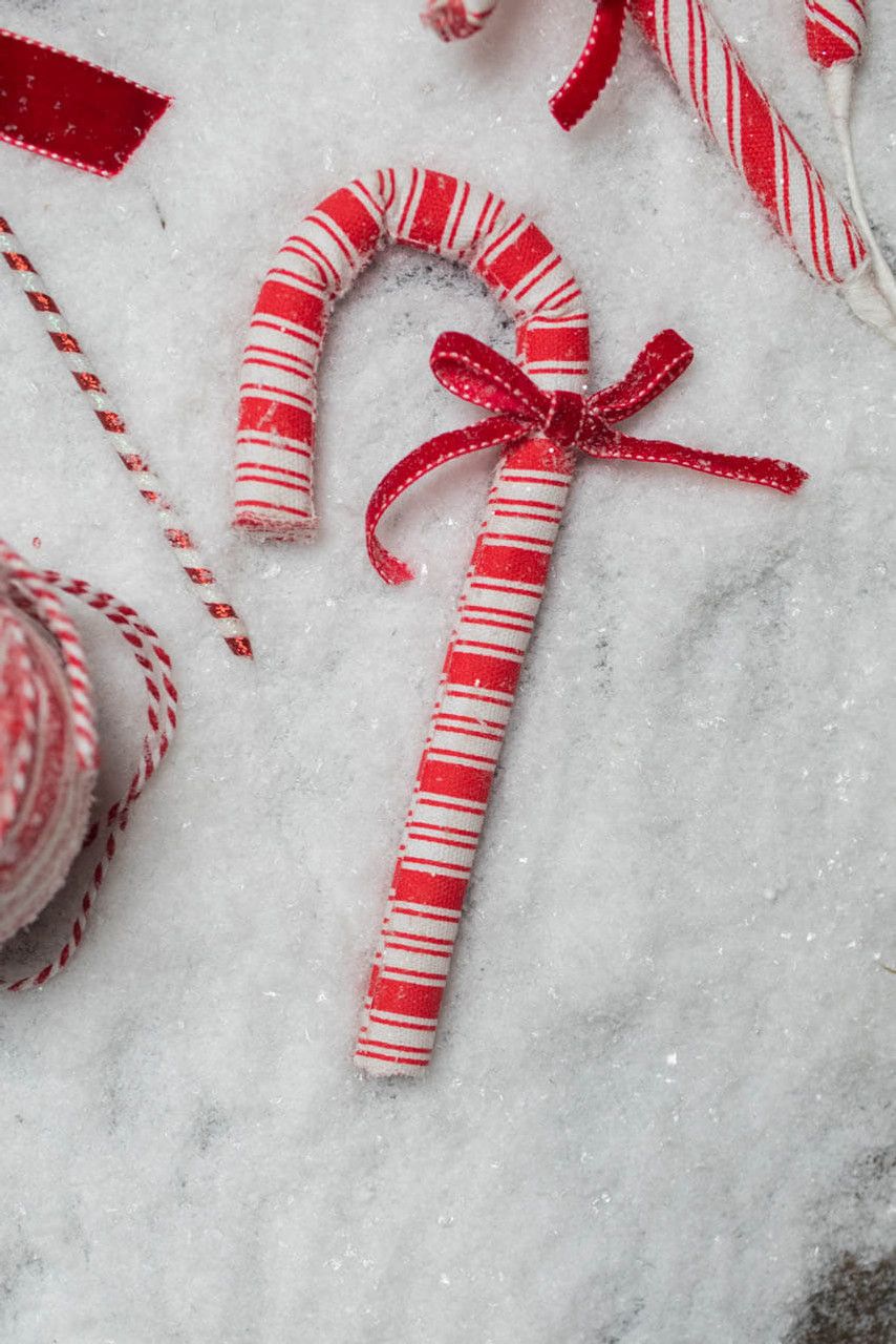A candy cane made out of yarn sitting on fake snow. - Candy cane