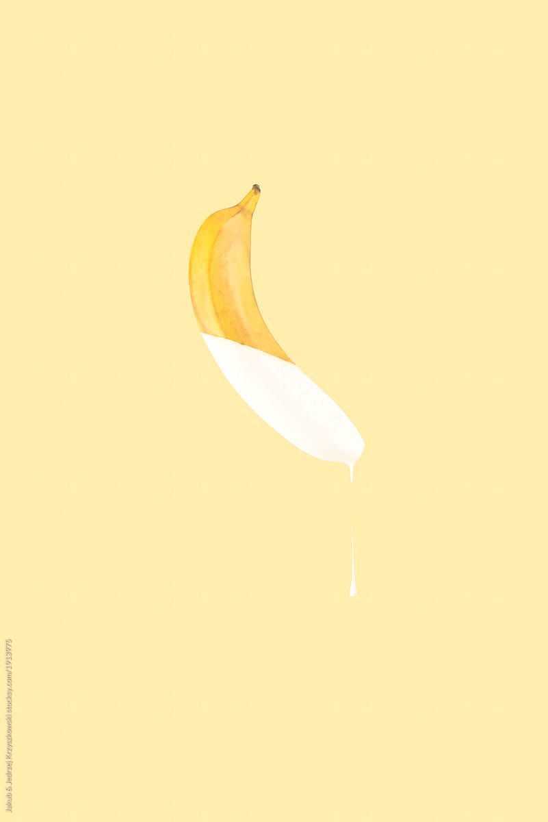 A banana that has been cut in half and is suspended in the air with milk dripping from it on a yellow background - Banana