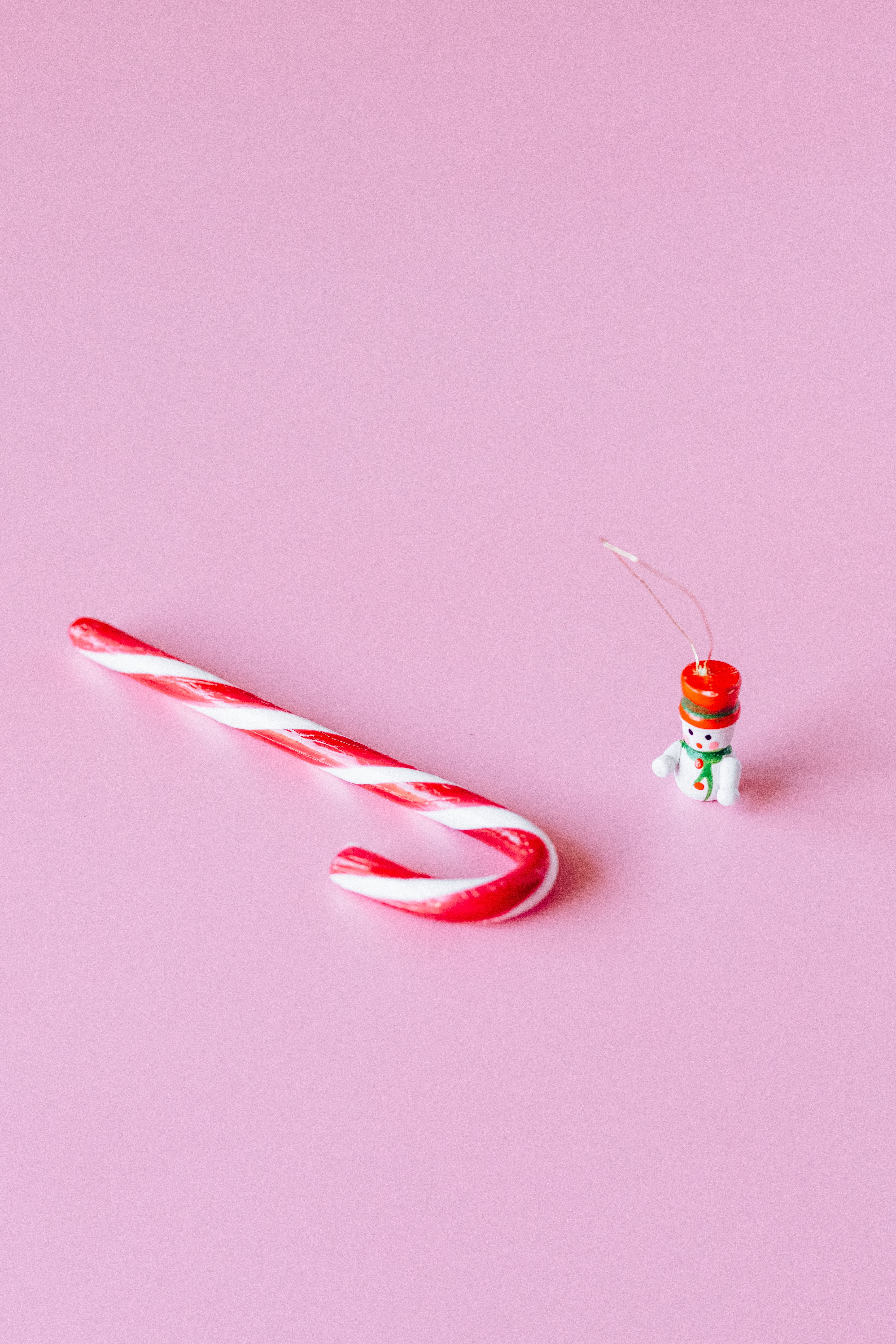 A candy cane and a small toy snowman on a pink background - Candy cane