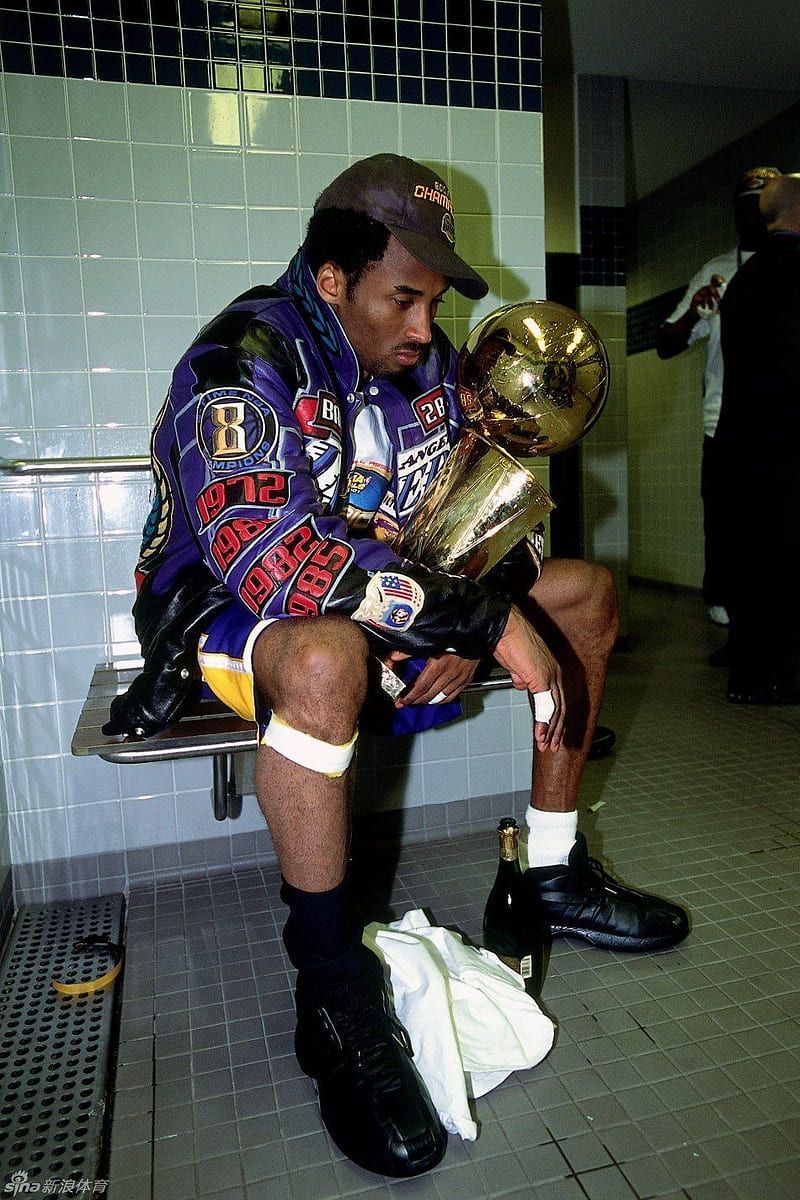 Kobe Bryant sitting on a bench holding a trophy - Kobe Bryant