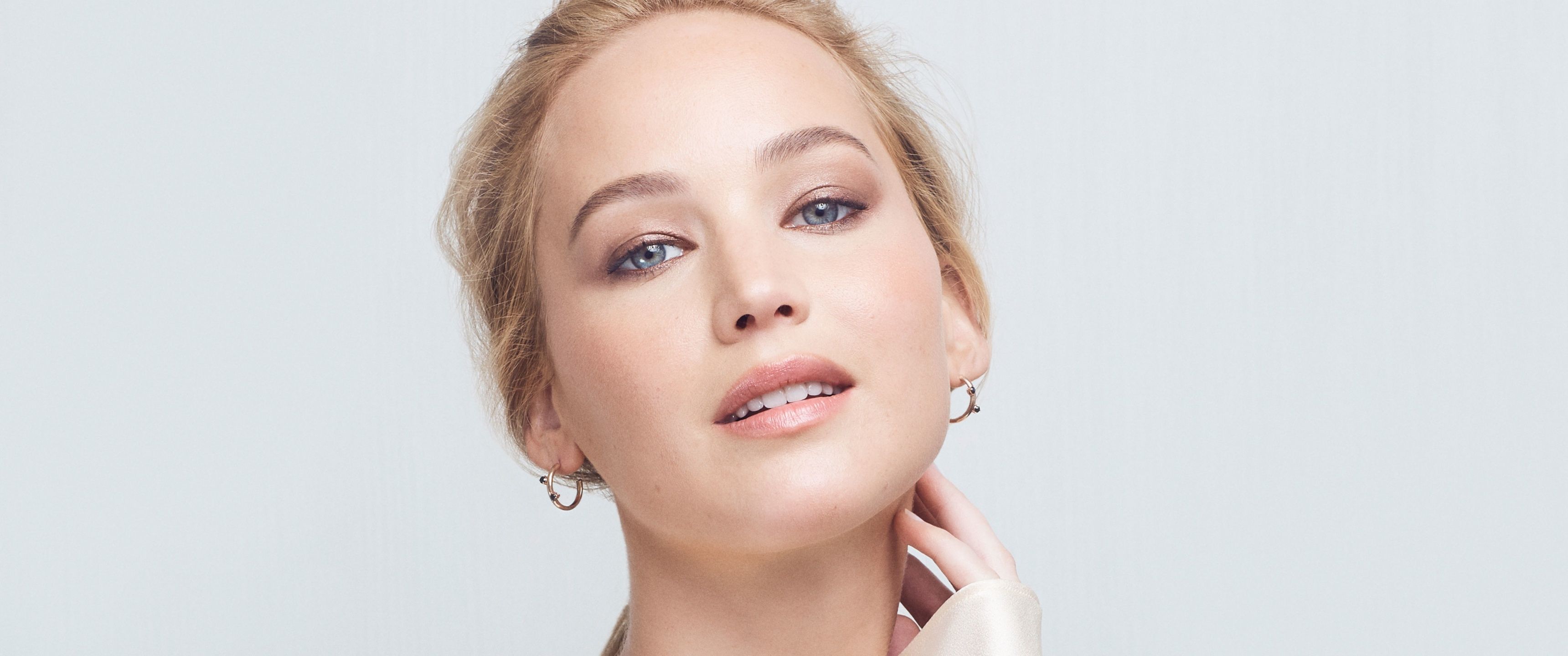 A woman with blonde hair and blue eyes wearing gold earrings. - Jennifer Lawrence