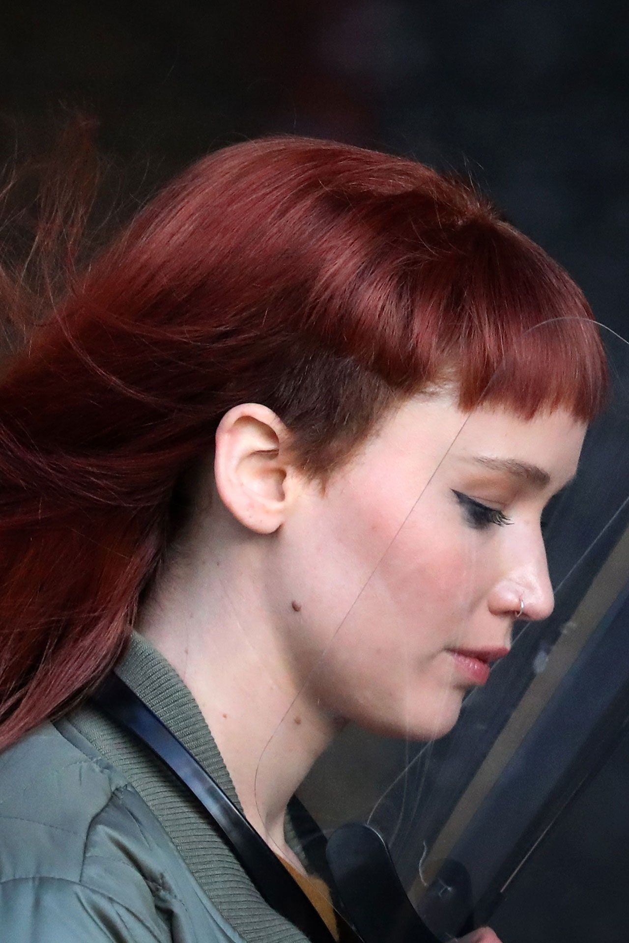 A woman with red hair and a nose ring looks down. - Jennifer Lawrence