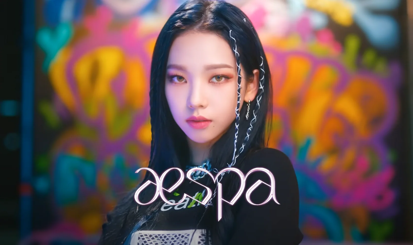 A blackpink member with long black hair, she is wearing a black top with the word JISPA written in white in front of her. - Aespa