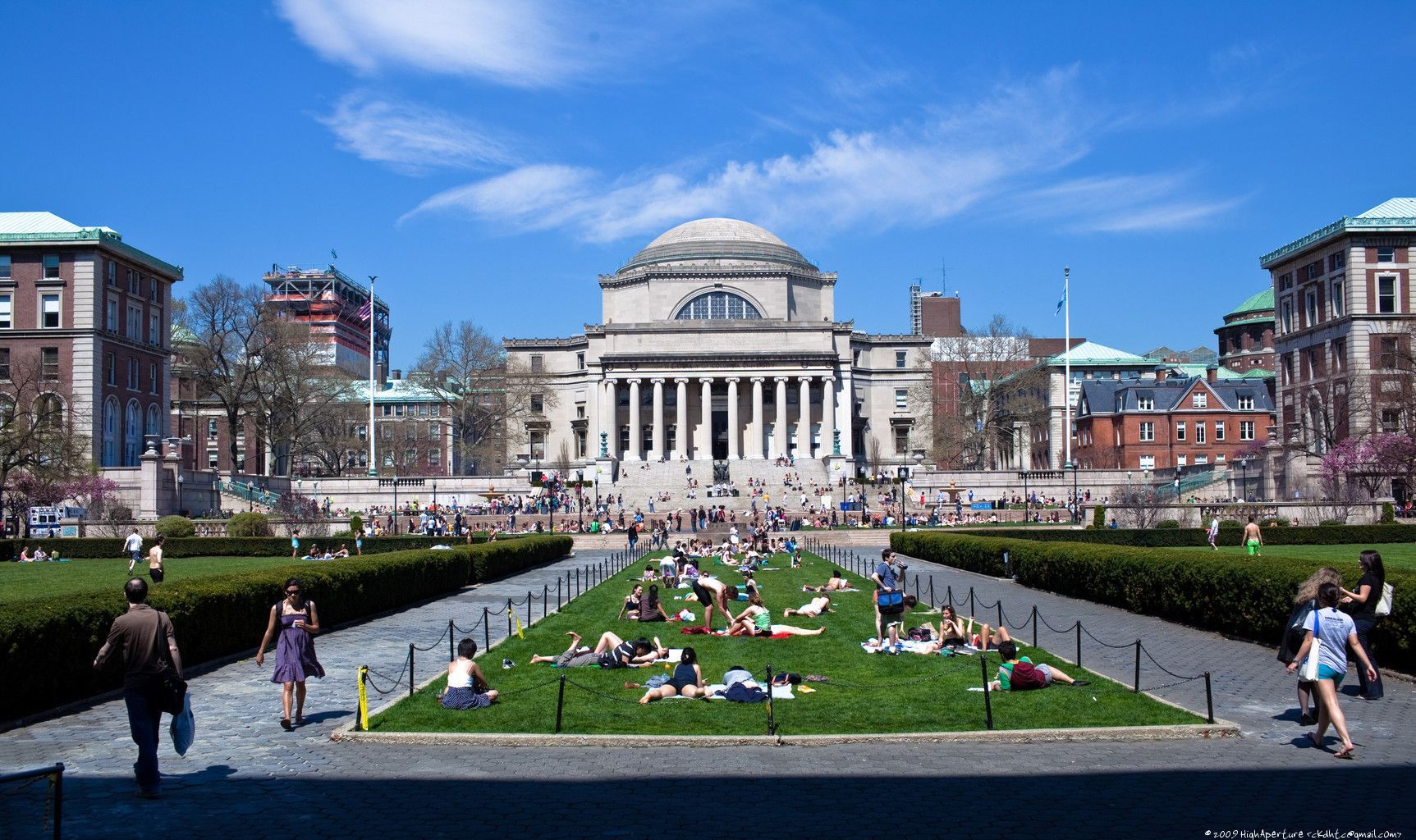People relaxing on the grass in front of a large building. - Columbia University