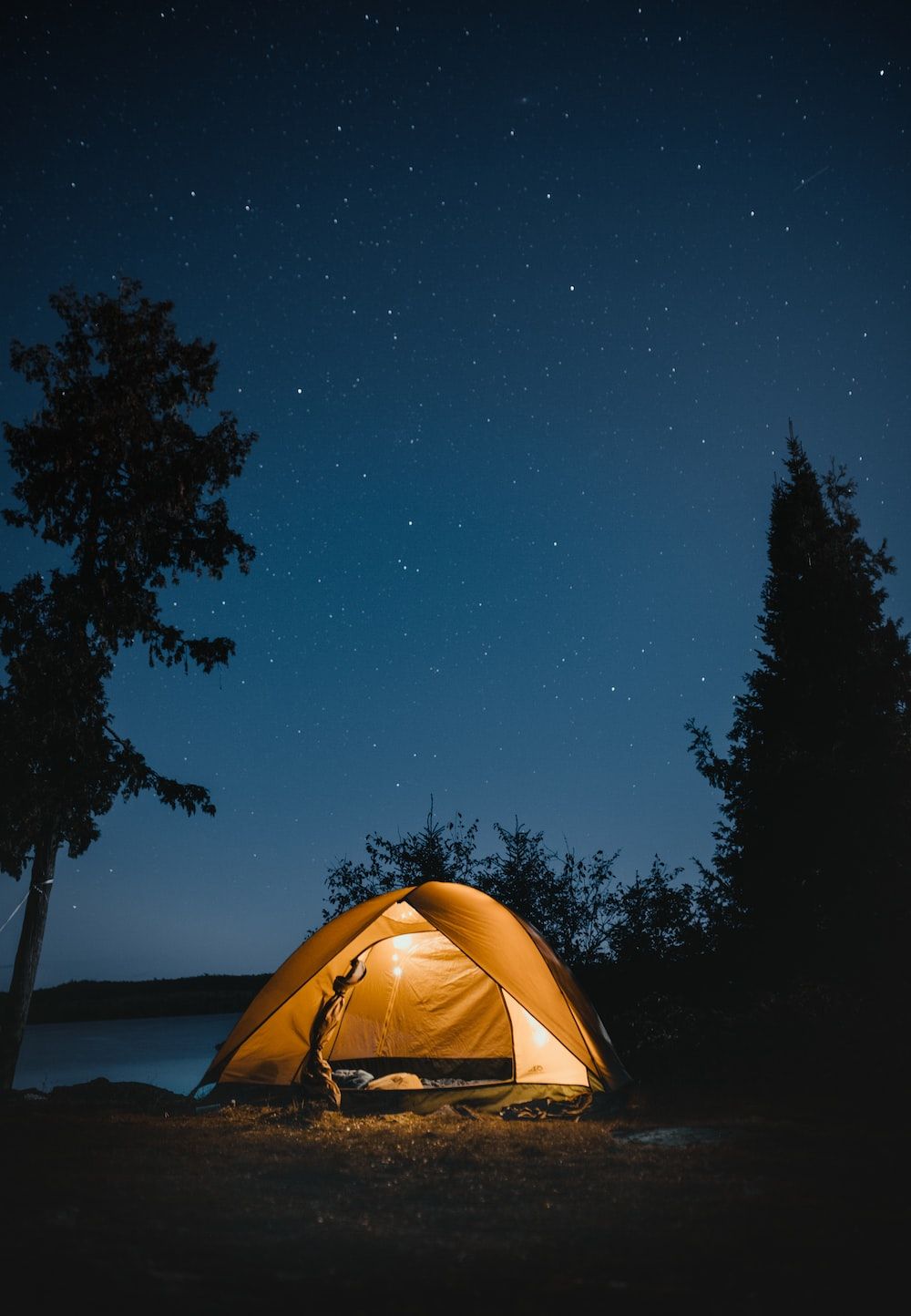 A cozy camping site under the night sky with a warm glow from the tent. - Camping