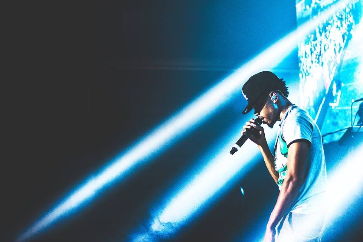 Chance the Rapper singing into a microphone on stage. - Chance the Rapper