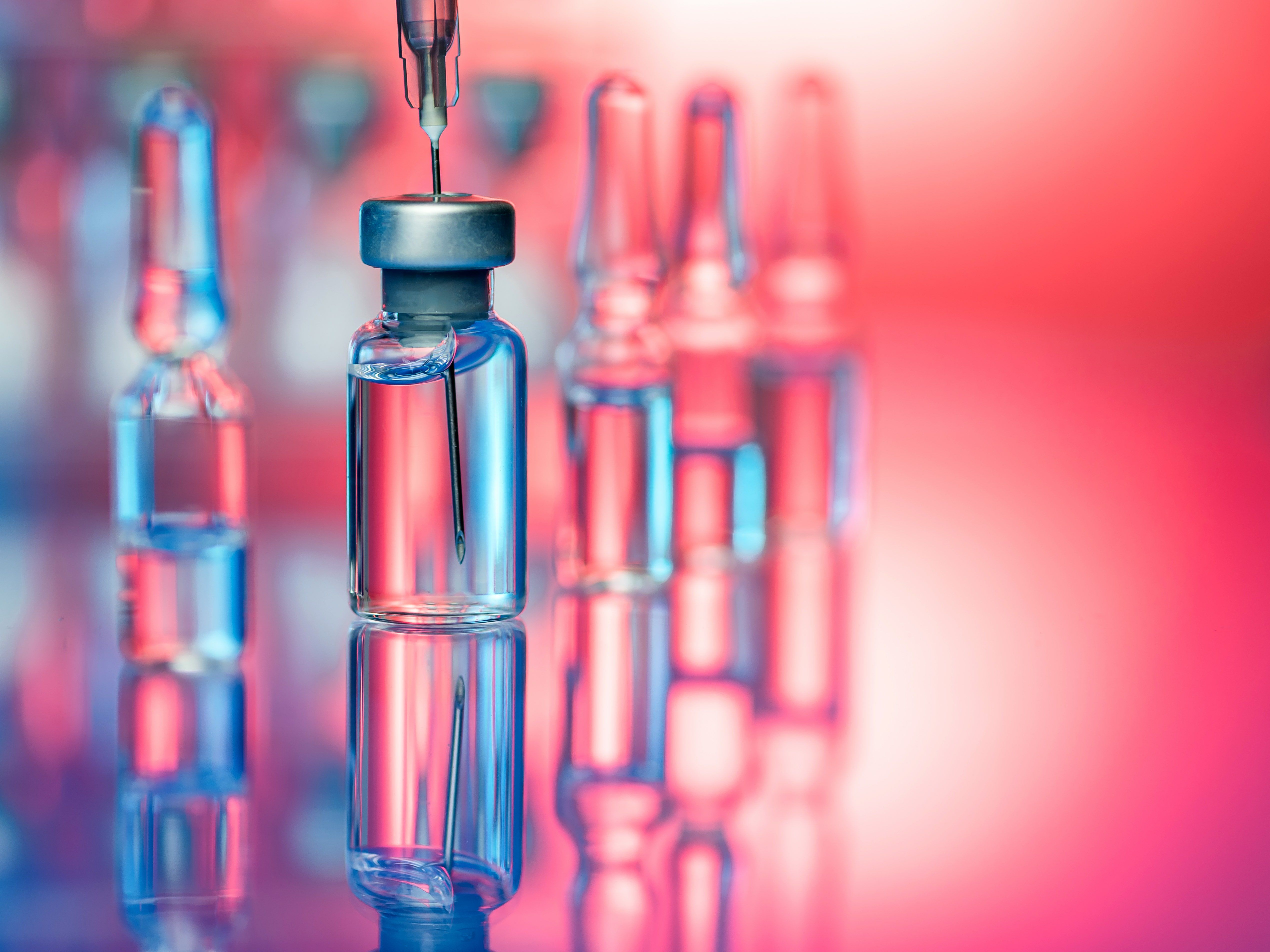 A row of vaccine bottles with one in the foreground being filled with a syringe - Chemistry
