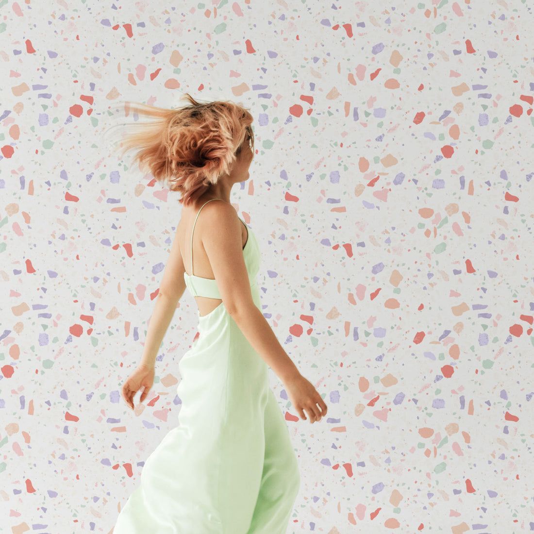 A woman in a green dress dances in front of a colorful wall. - Terrazzo