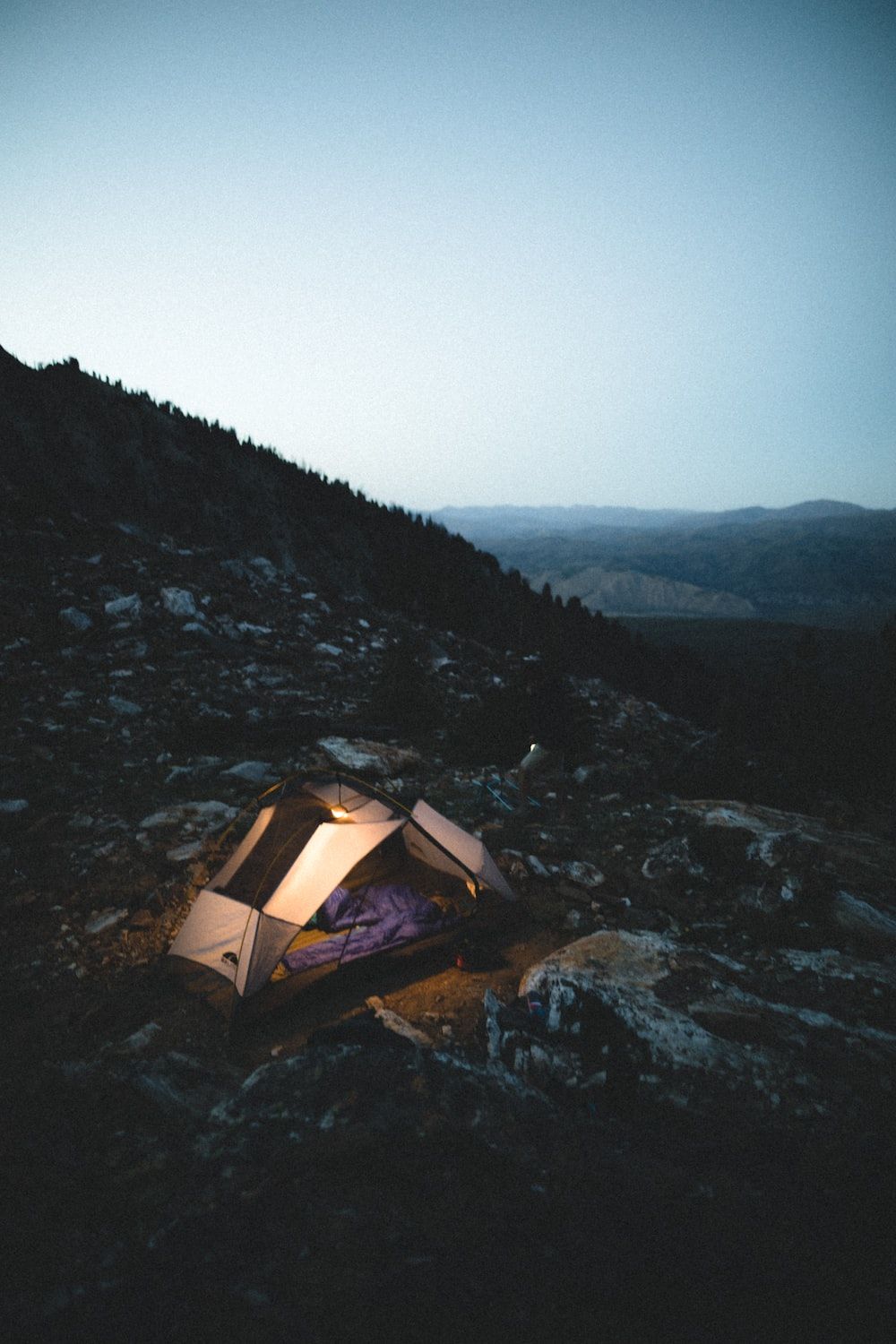 A tent pitched on a rocky hillside at dusk. - Camping