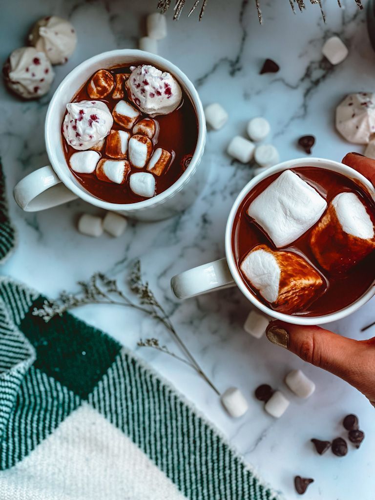 Two cups of hot chocolate with marshmallows and a hand holding one of the cups - Chocolate, marshmallows