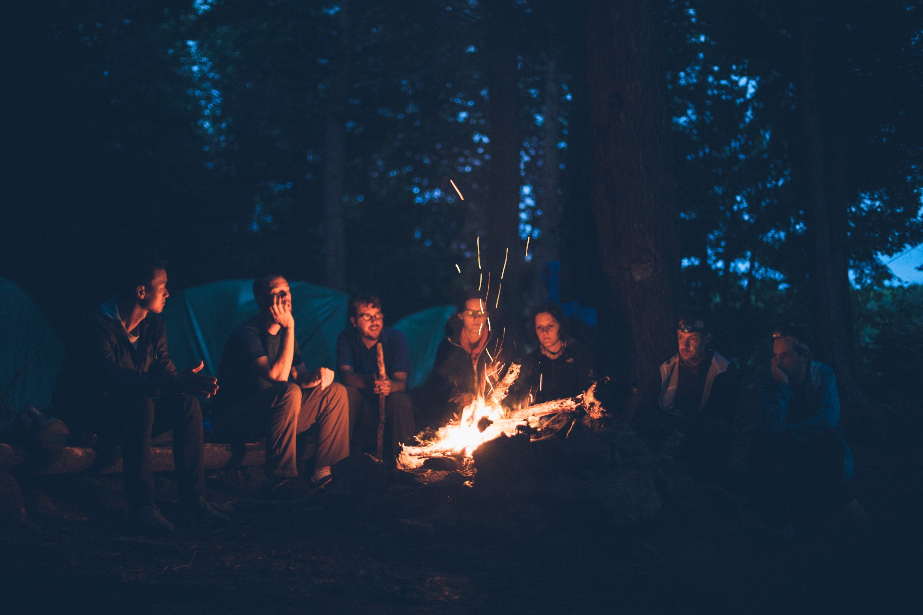A group of people sit around a campfire at night. - Camping