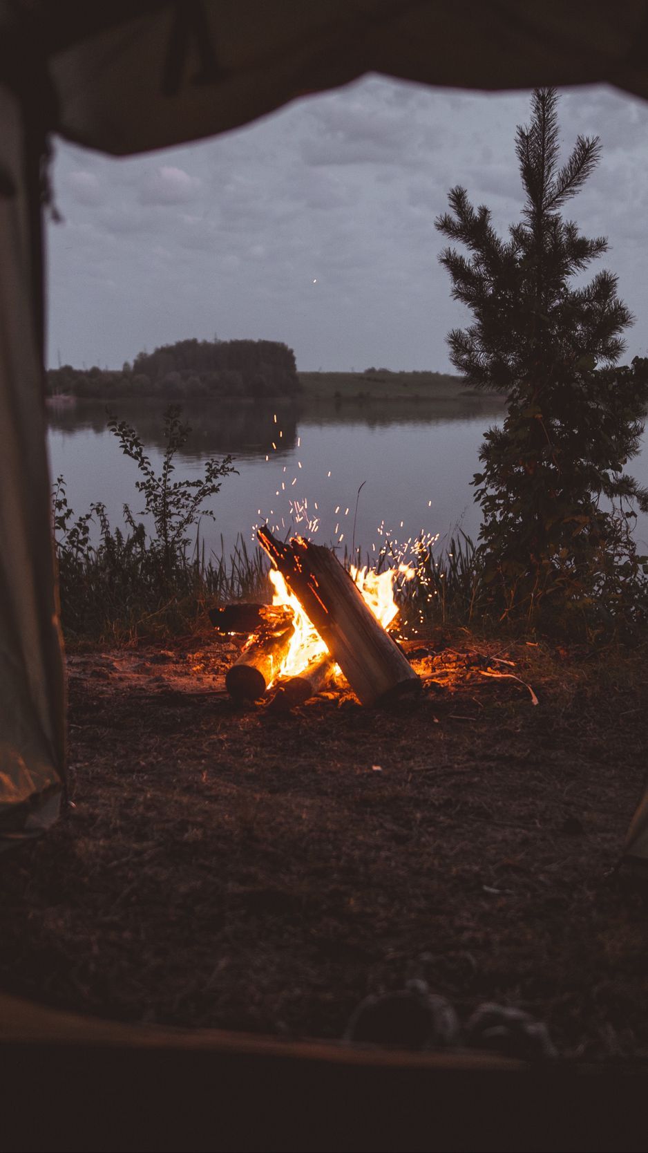 A campfire in the woods with water nearby - Camping