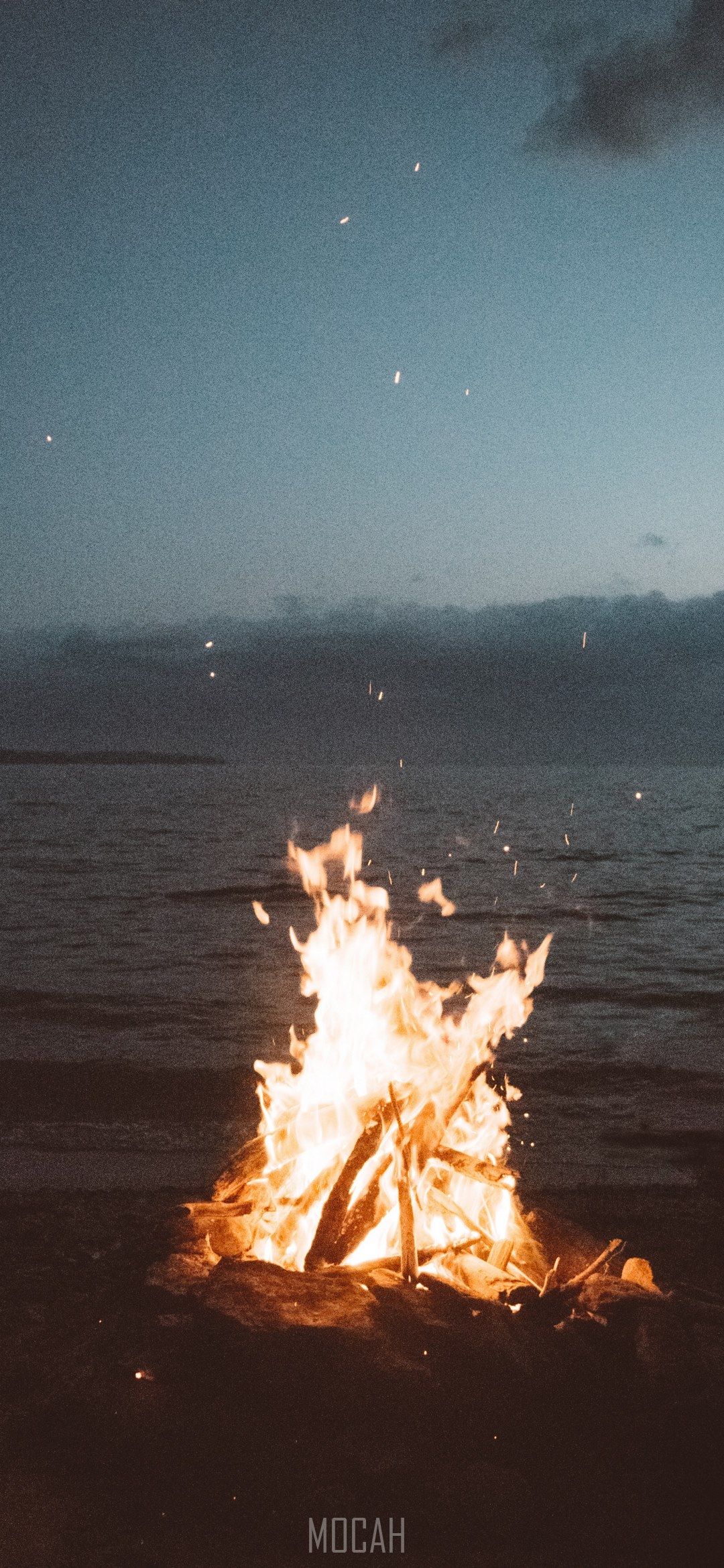 A bonfire burns on the beach with the ocean in the background - Camping
