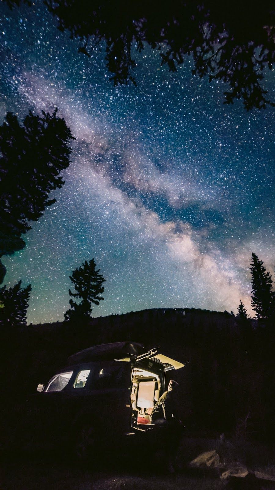 A van is parked under a starry sky with a campfire in the woods. - Camping